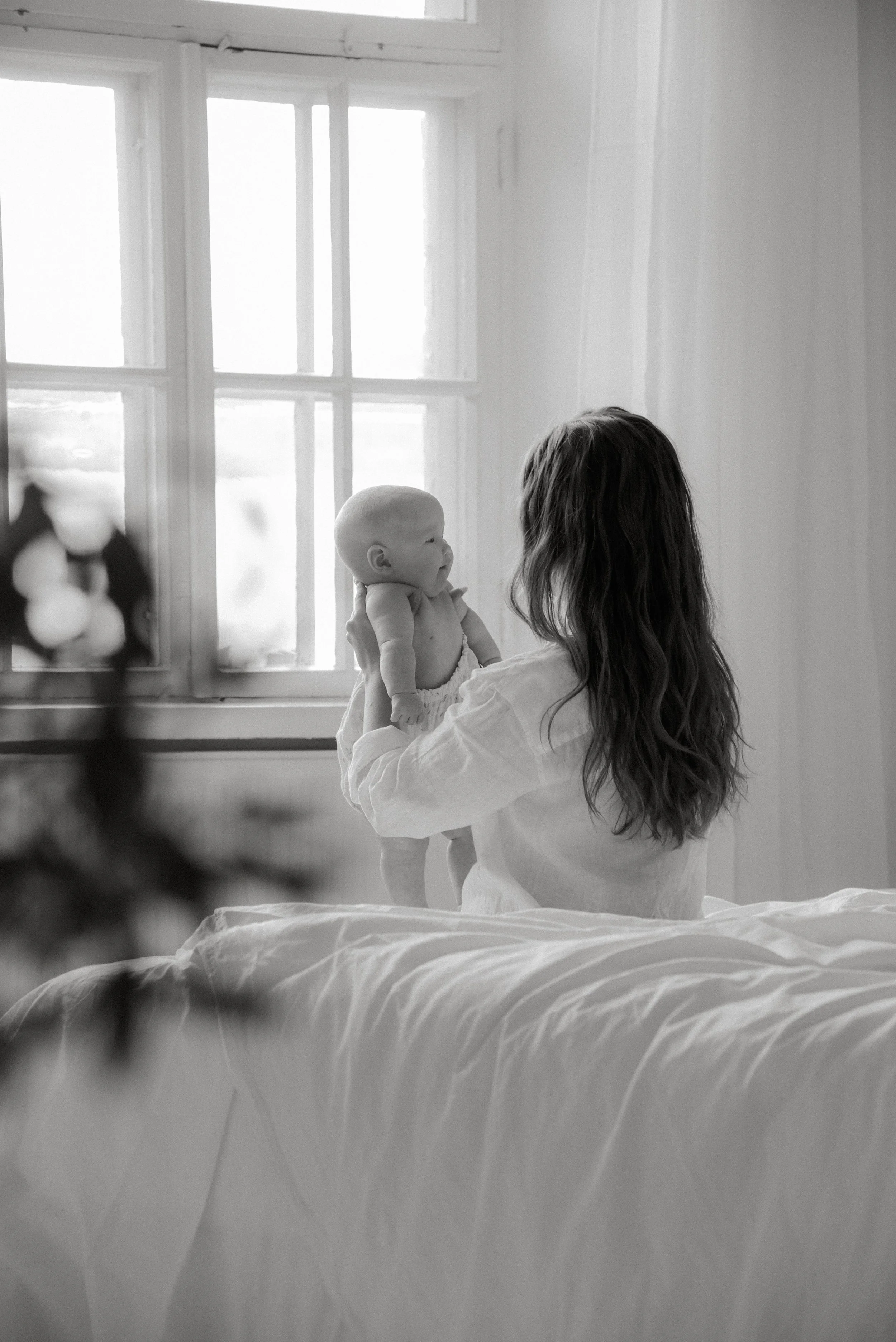 Valoa tulvii ikkunoista Keravan studiolle. Äiti pitää vauvaa sylissään sängyllä istuen.