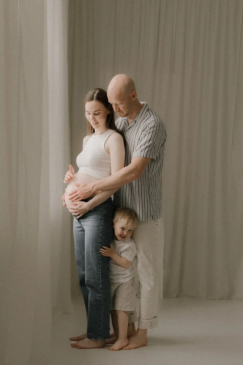 Lämminhenkinen perhekuva, jossa isä ja lapsi halaavat raskaana olevaa äitiä.