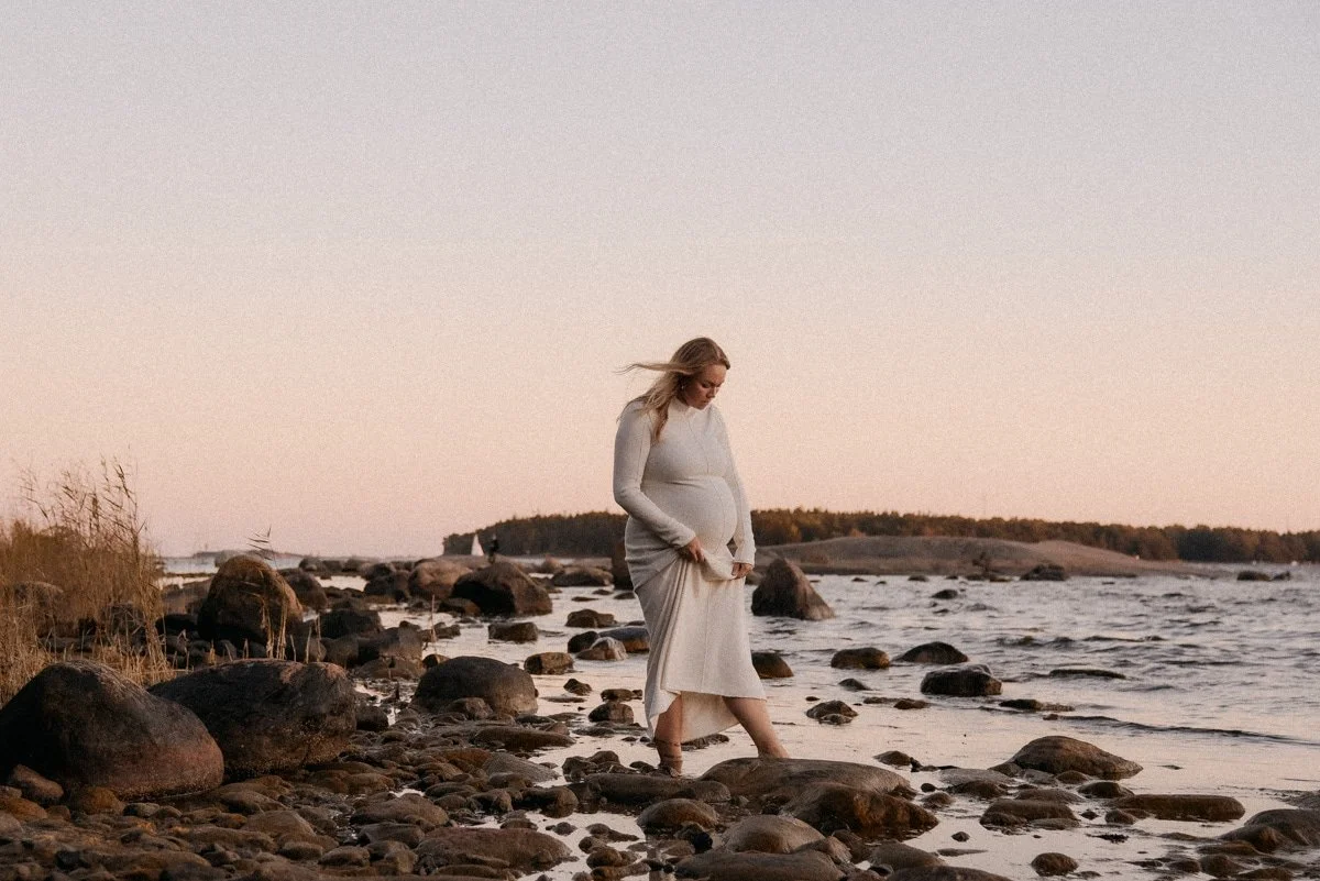Odotusajan kuvaus, raskaana oleva äiti kuvattavana meren rannalla ilta-auringossa.