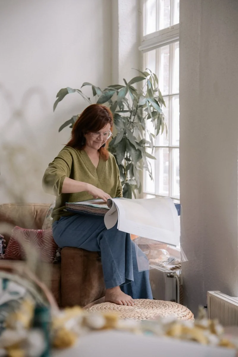 Verhoomo Vanhan Viehätys yrityskuvaus, yrittäjä Virve Taljavirta istuu ikkunan ääressä ja pitelee käsissään kangasnäytteitä.