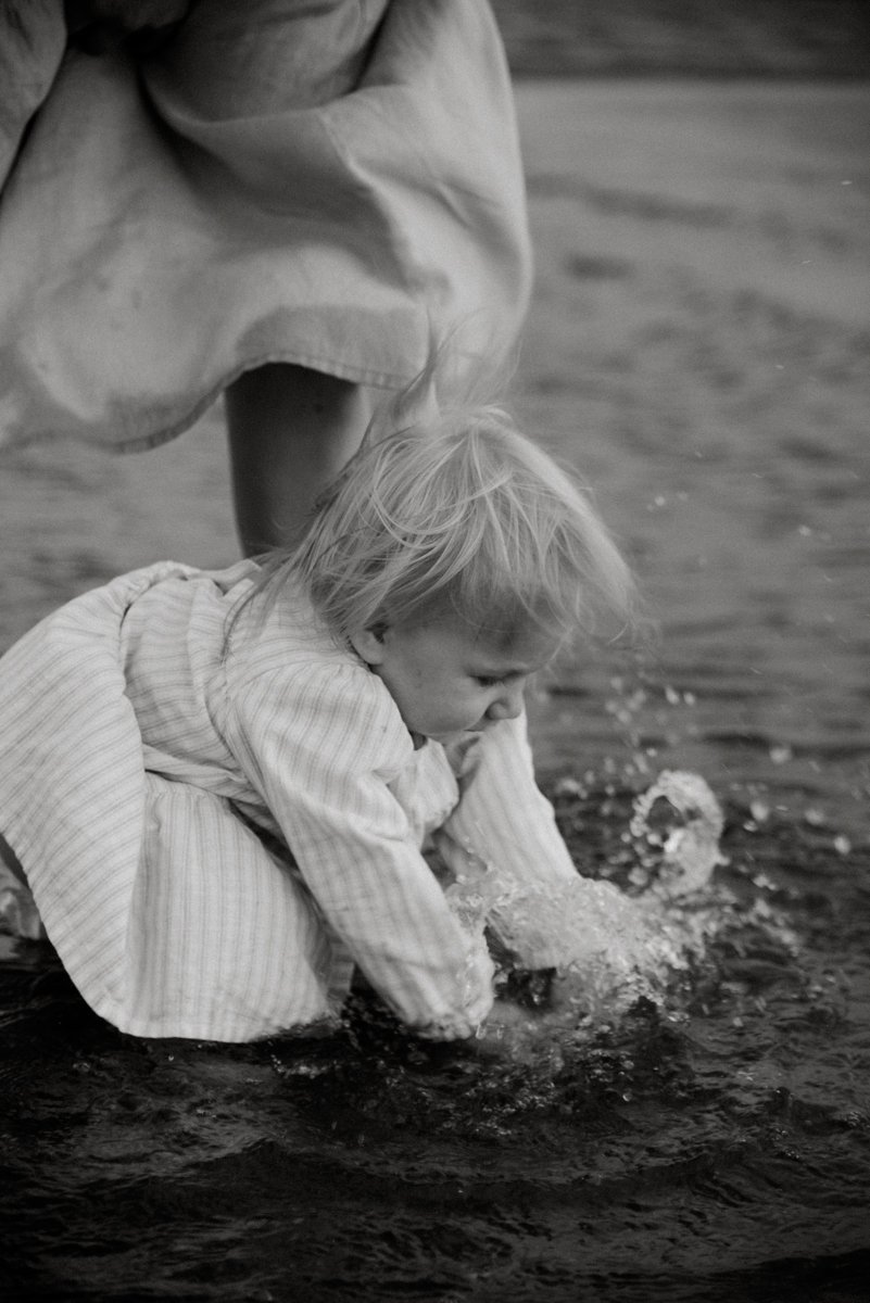 Mustavalkoinen perhekuva, lapsi leikkii vedessä äidin vieressä.