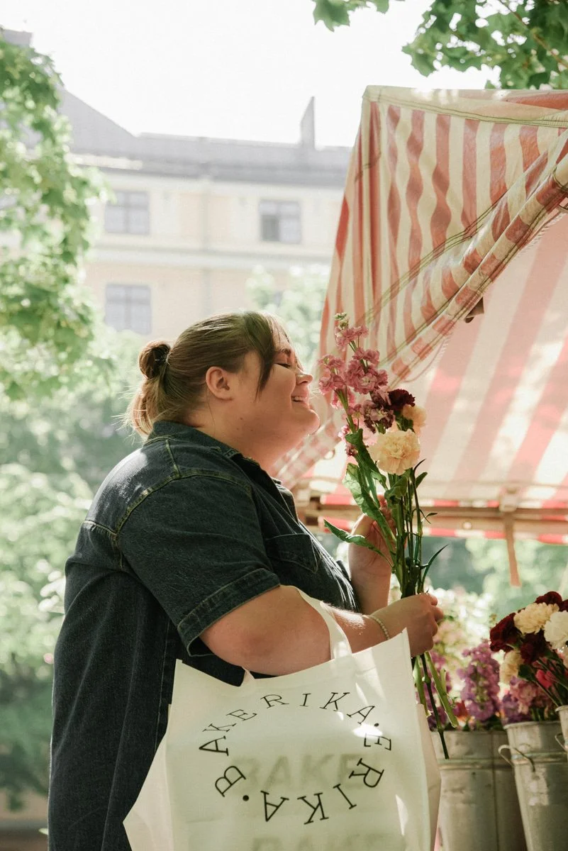Kaupunkimiljöössä toteutettu Bakerikan brändikuvaus. Yrittäjä seisoo torilla kukkia käsissään.