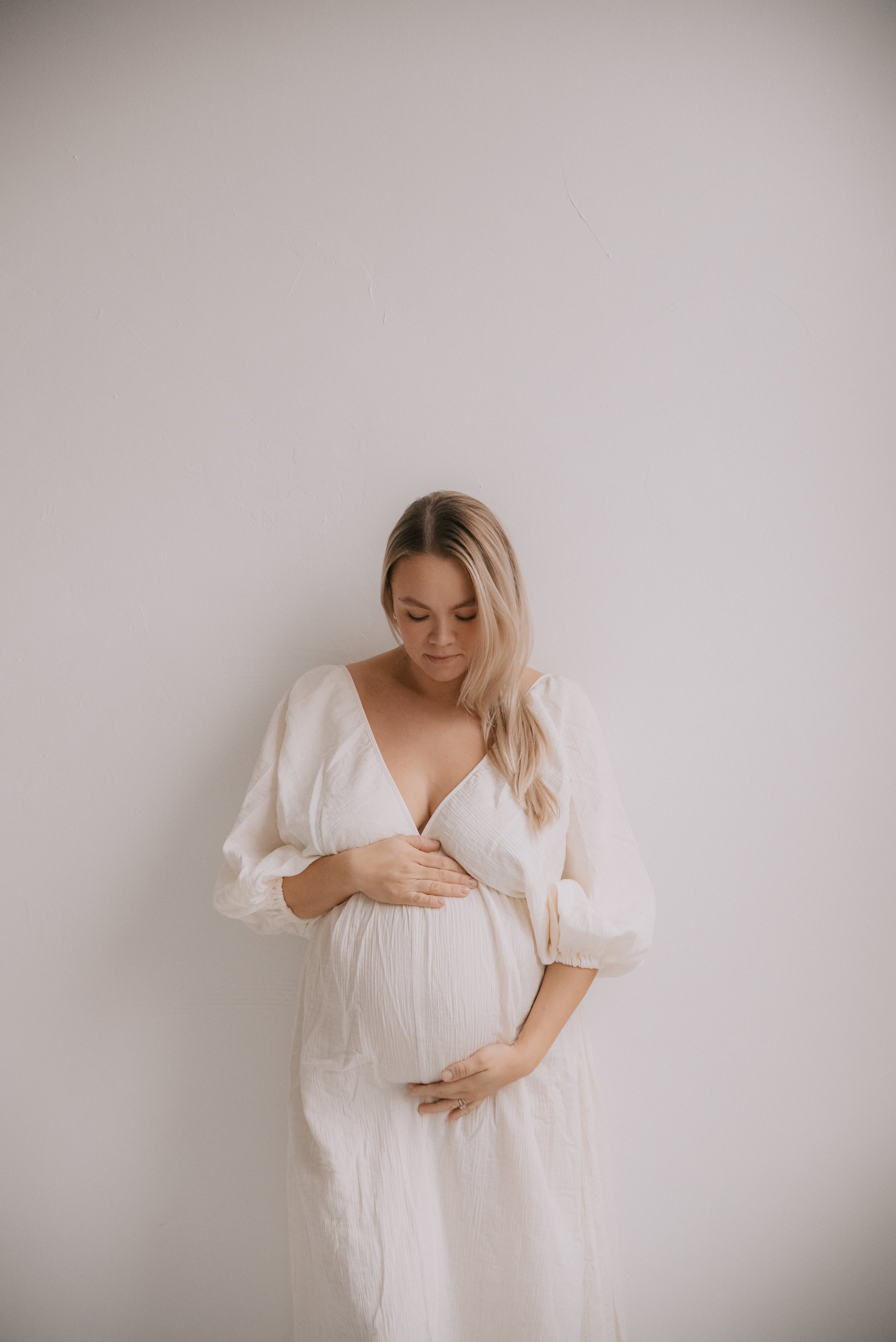 Vaaleasävyisessä kuvassa odottava äiti katsoo vatsaansa. Odotusajankuvaus Heidi Väisäsen studiolla Saviossa.