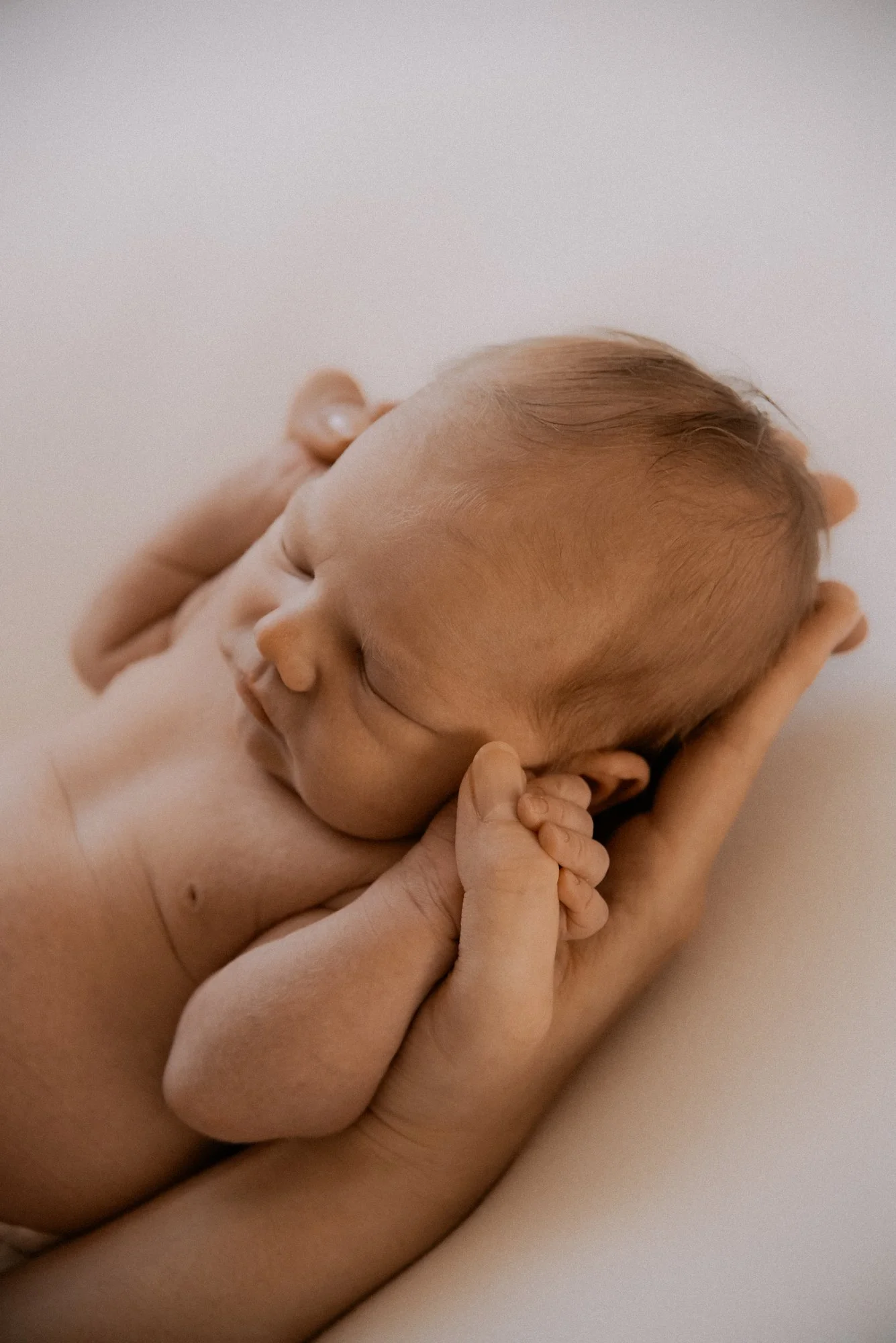 Pieni vauva nukkuu ja pitelee vanhemman peukalosta. Kuvan on ottanut vauvakuvaaja Heidi Väisänen.