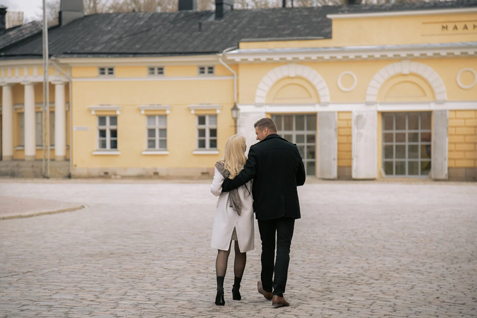 Mies ja nainen kävelevät keltaisen talon edessä. Pariskuntakuvaus Helsinki.