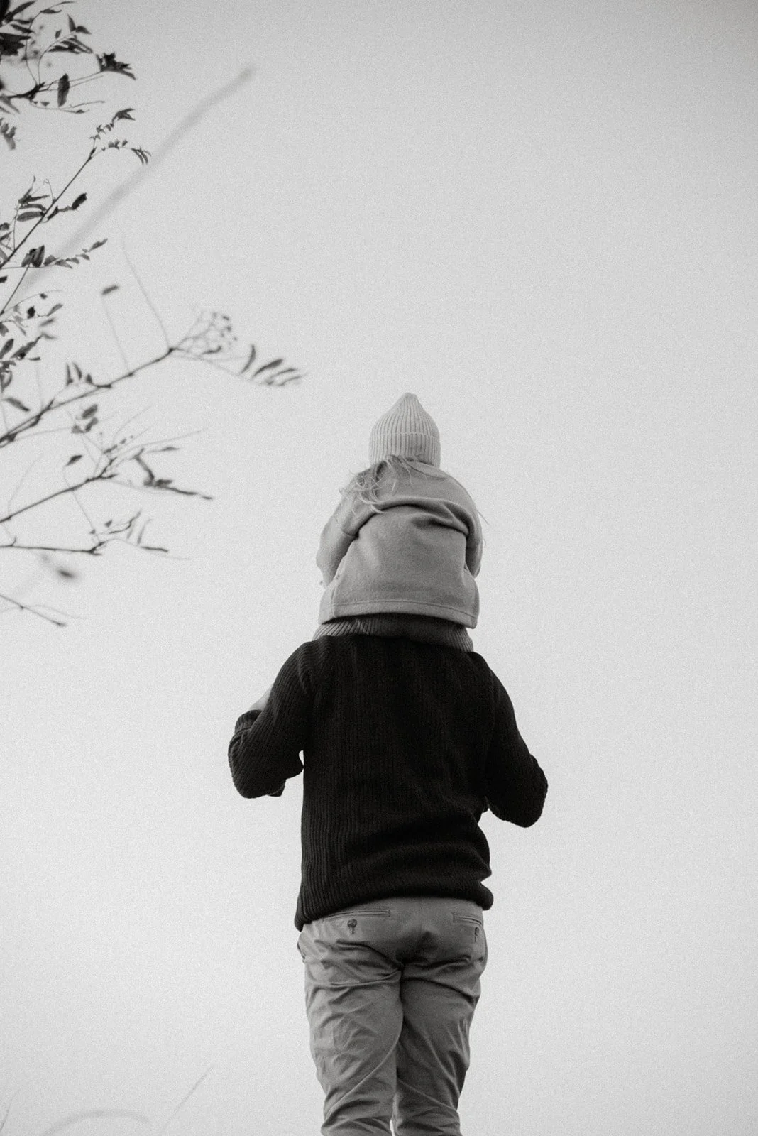 Mustavalkoinen perhekuva, lapsi isän hartioilla.