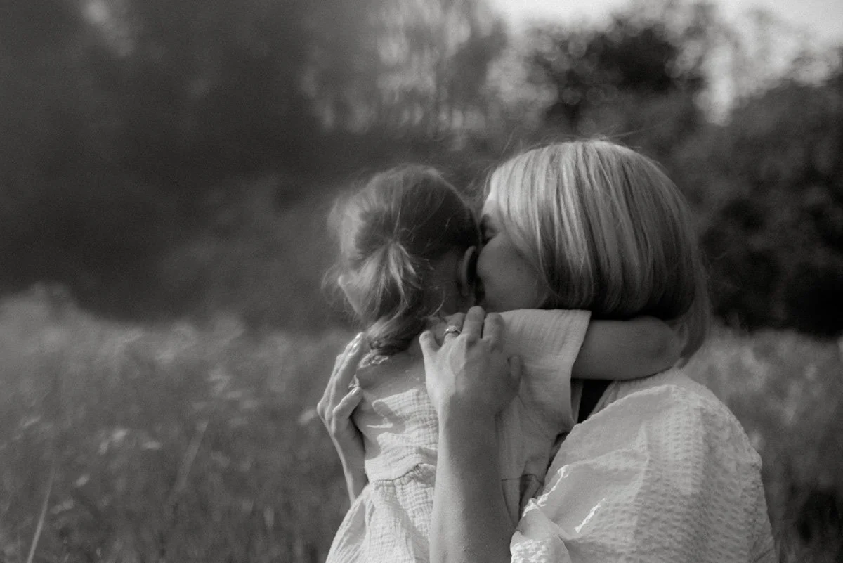 Perhekuvaus luontomaisemassa, äiti halaa lasta.