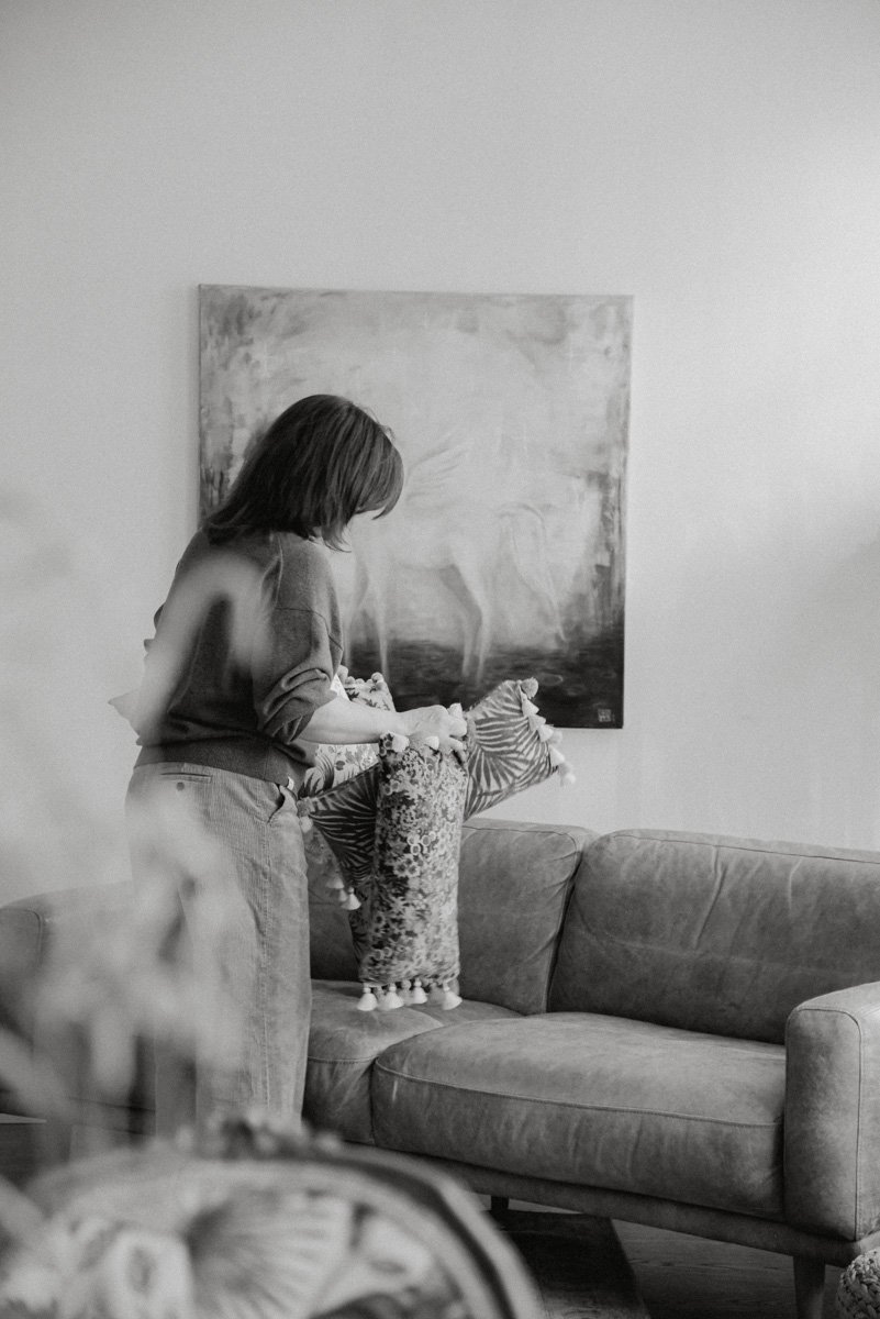 Verhoomo Vanhan Viehätys brändikuvaus, mustavalkoinen kuva yrittäjä Virve Taljavirtasta asettelemassa tyynyjä sohvalle.