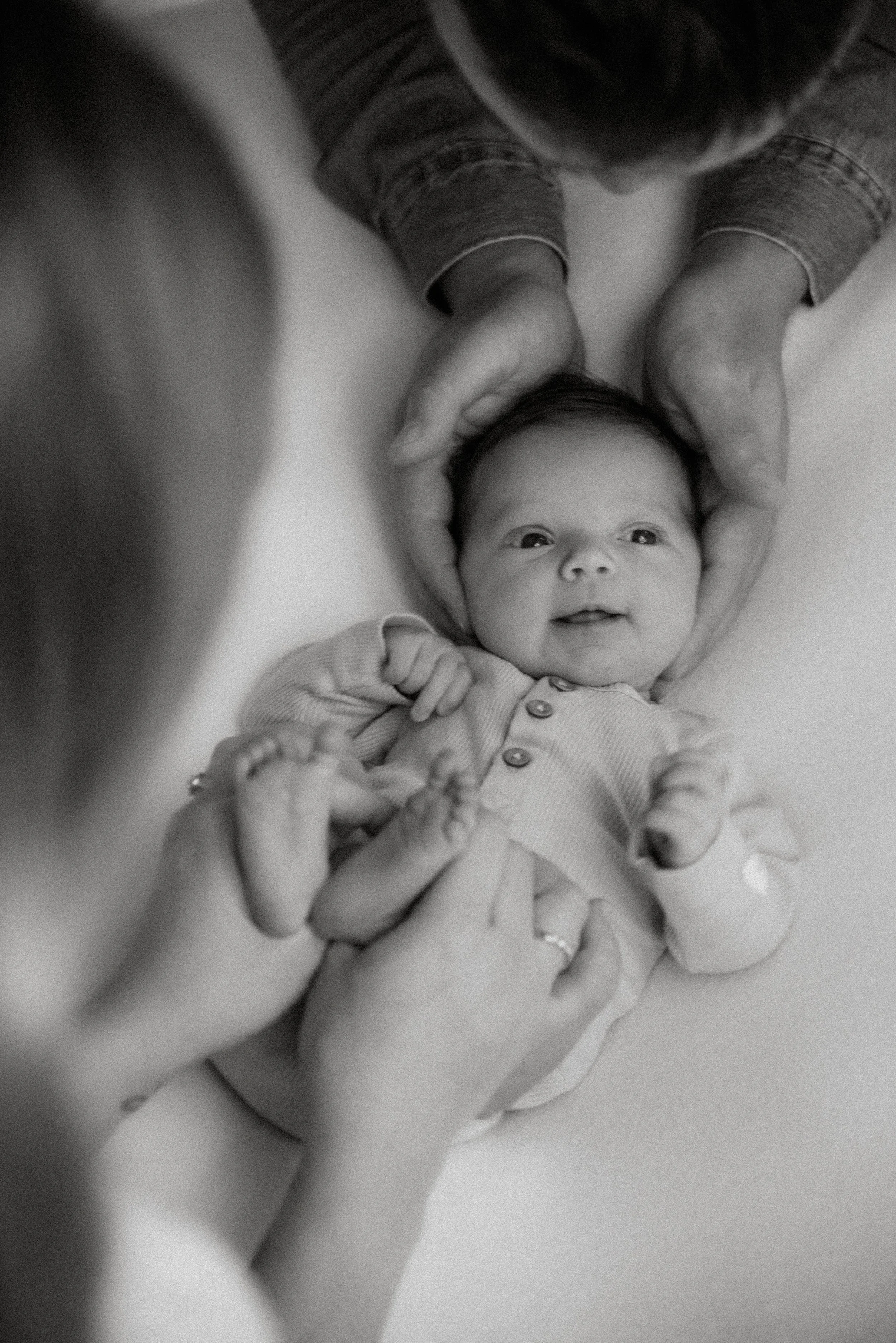 Iloinen vastasyntynyt vanhempien hellässä kosketuksessa. Kuvan on ottanut vauvakuvaaja Heidi Väisänen.