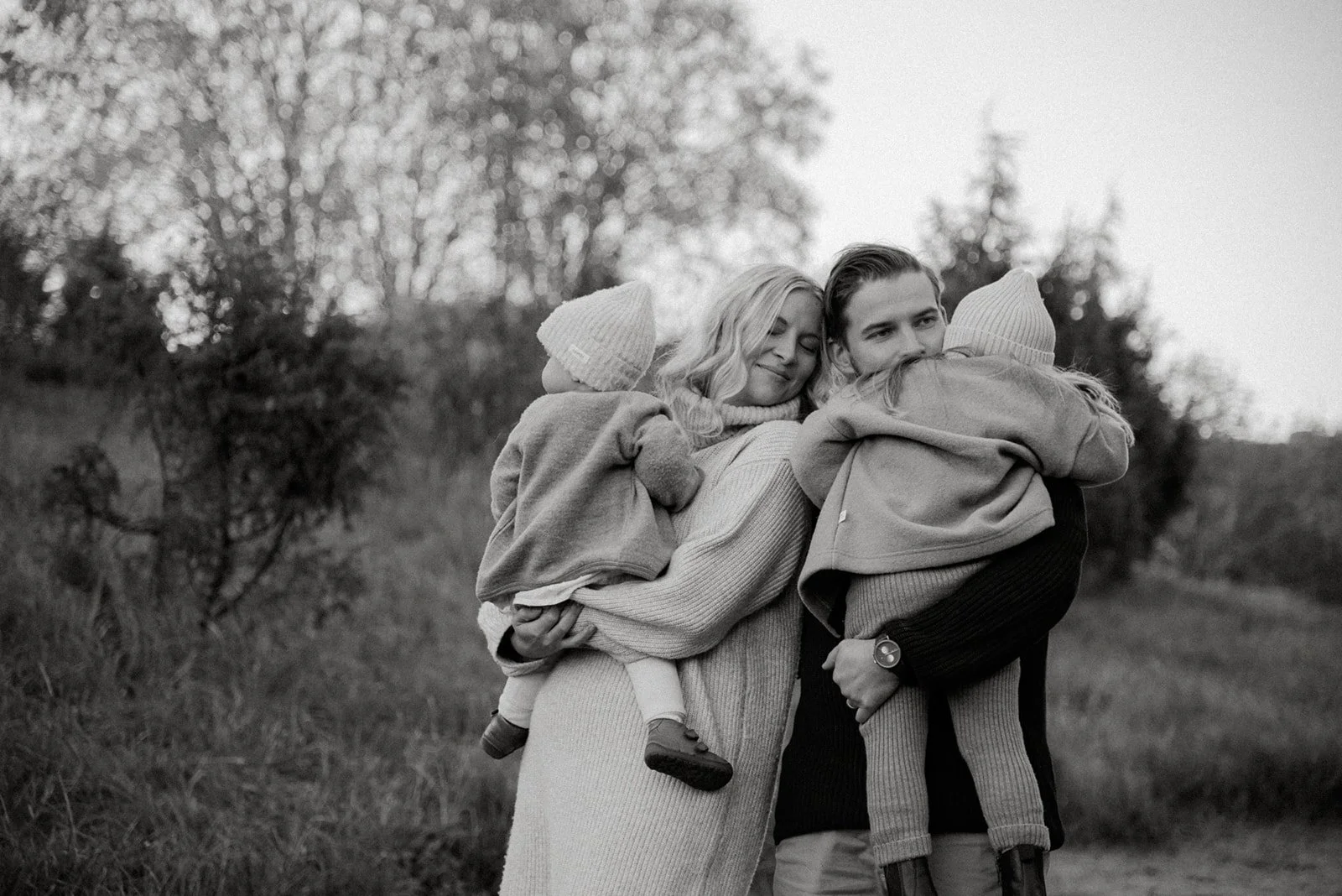 Perhekuvaus miljöössä, äiti ja isä, molemmilla lapsi sylissään. Kuvannut valokuvaaja Heidi Väisänen.