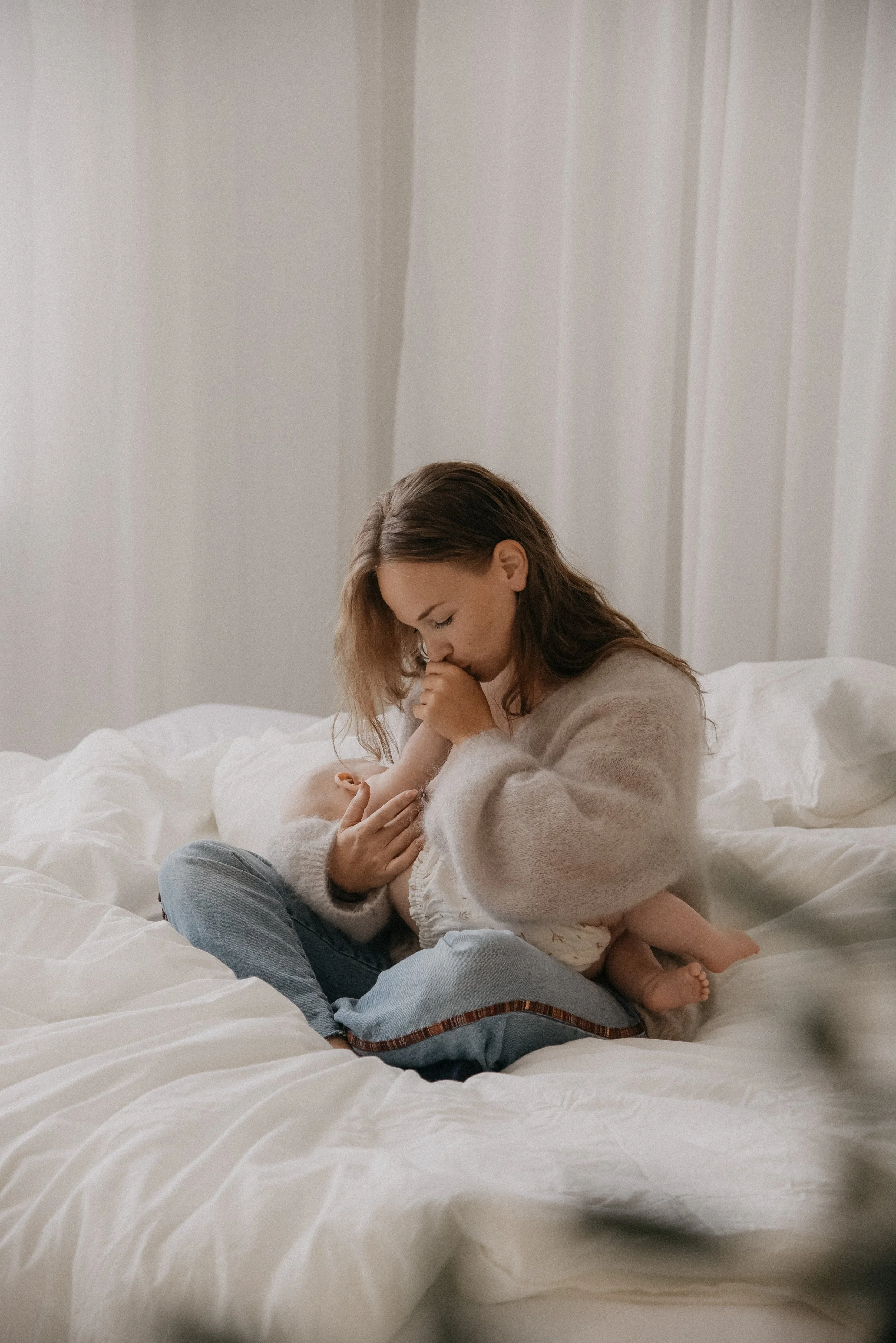 Äiti ja lapsikuva, jossa äiti pitää vauvaa sylissä sängyllä istuen.
