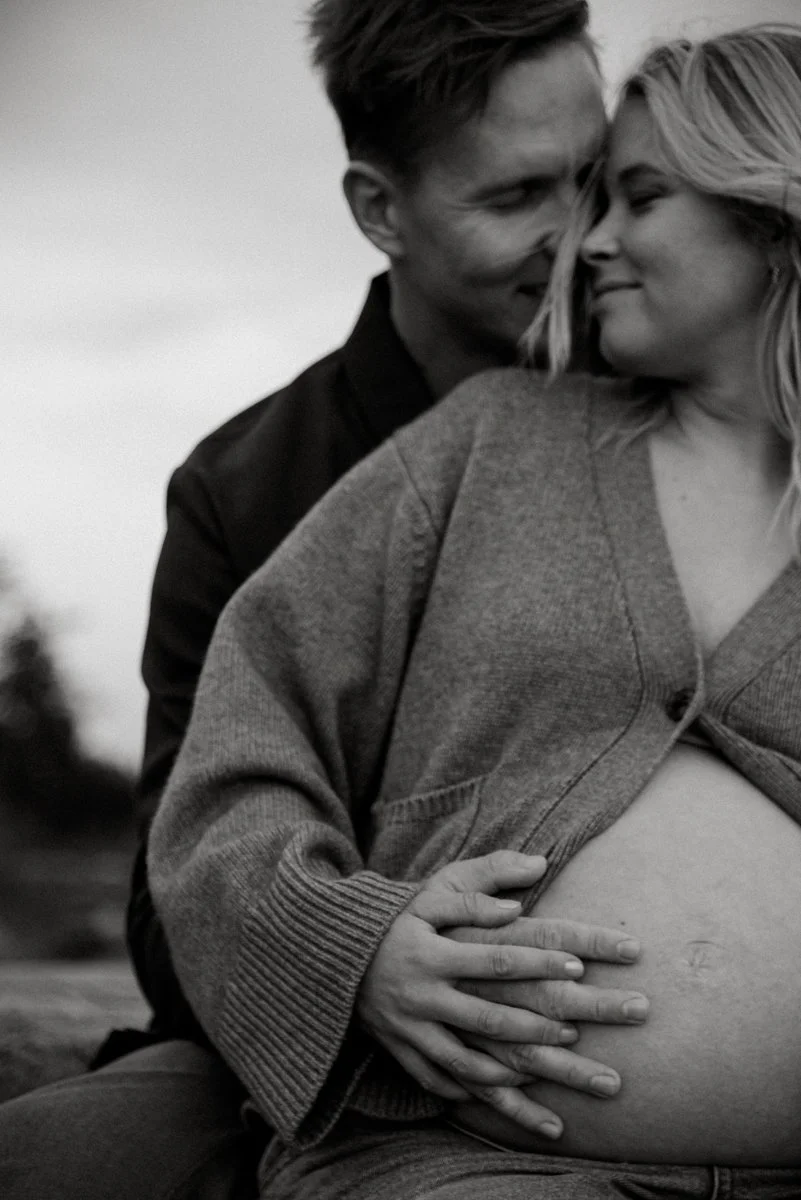 Puoliso koskettaa tulevan äidin vatsaa hellästi. Kuvannut raskausajankuvaaja Heidi Väisänen.