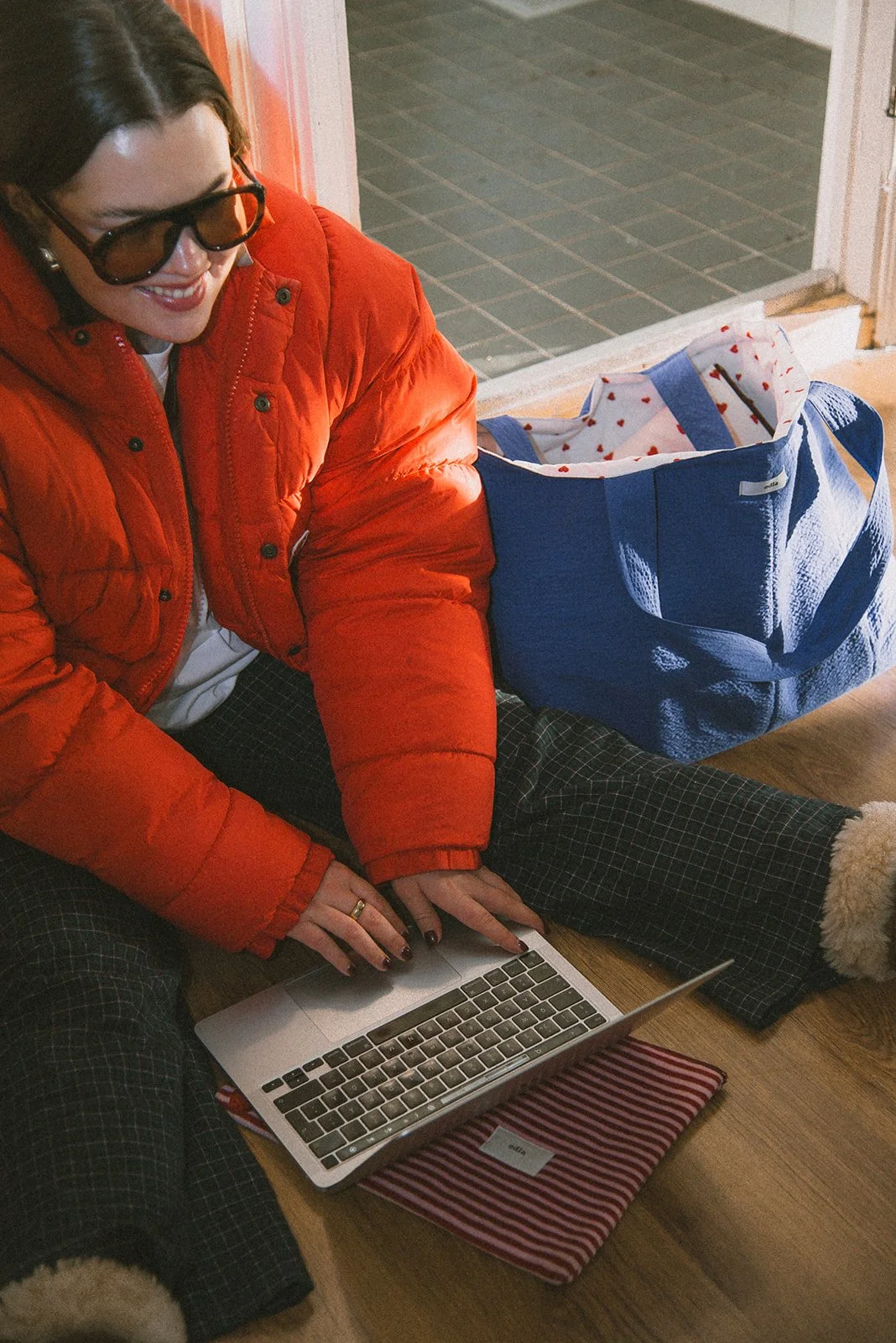 Edlan yrityskuvaus, yrittäjä istuu lattialla ja näpyttelee tietokonetta, vieressä brändin laukku.