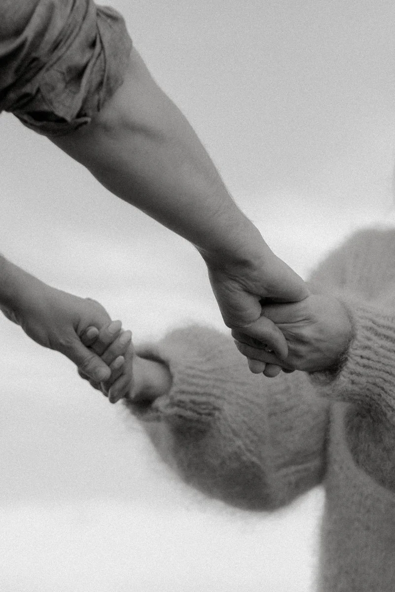 Mustavalkoinen kuva, jossa vanhempi pitää lastaan molemmista käsistä.