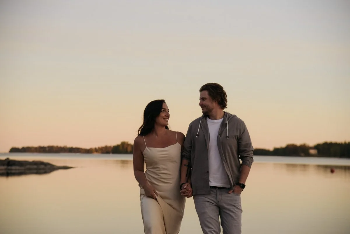 Pariskunta seisoo käsi kädessä tyynessä kesäillassa. Pariskuntakuvaus pääkaupunkiseutu. Valokuvaaja Heidi Väisänen.