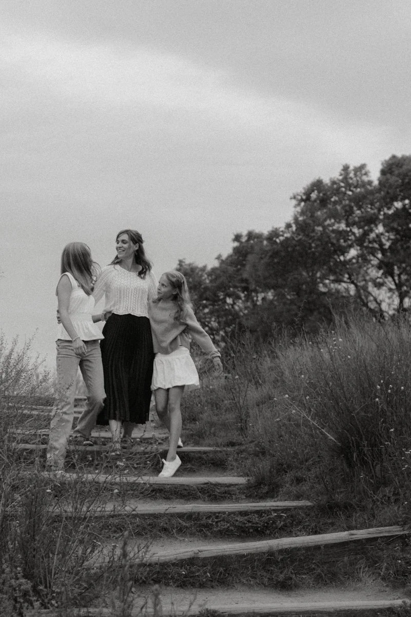 Perhekuvaus Helsinki, äiti ja tyttäret kävelevät portaita luonnossa.