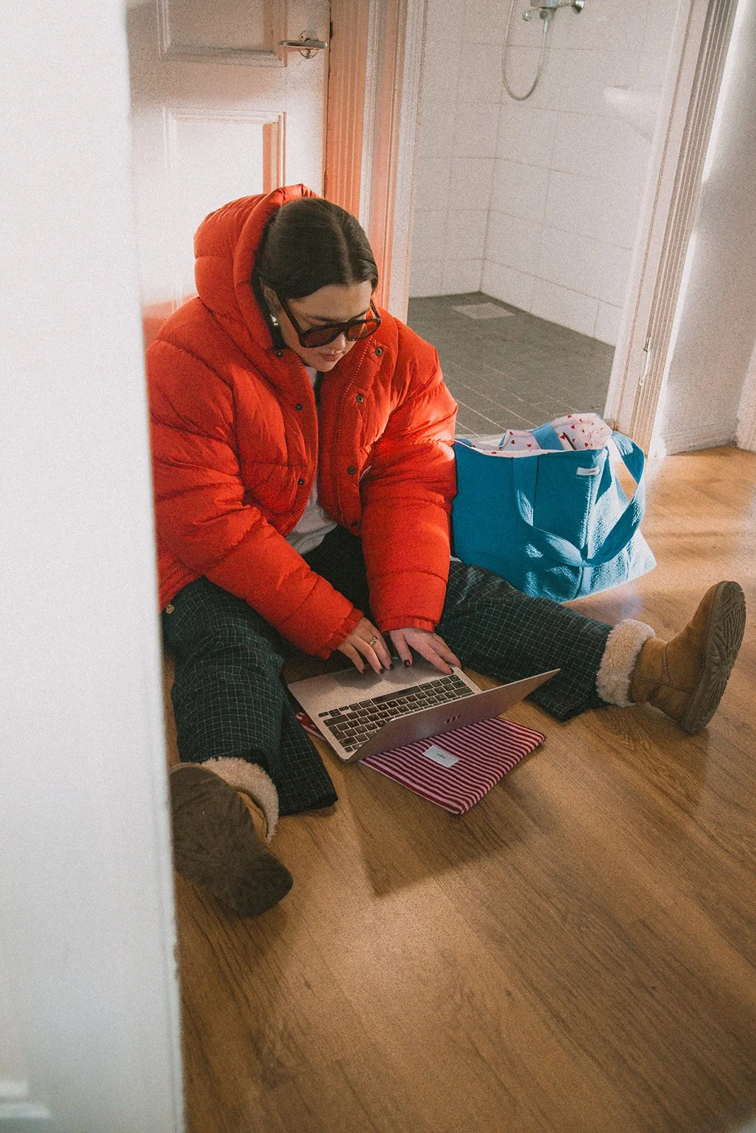 Edlan brändikuvaus, yrittäjä istuu lattialla ja näpyttelee tietokonetta, vieressä brändin laukku.