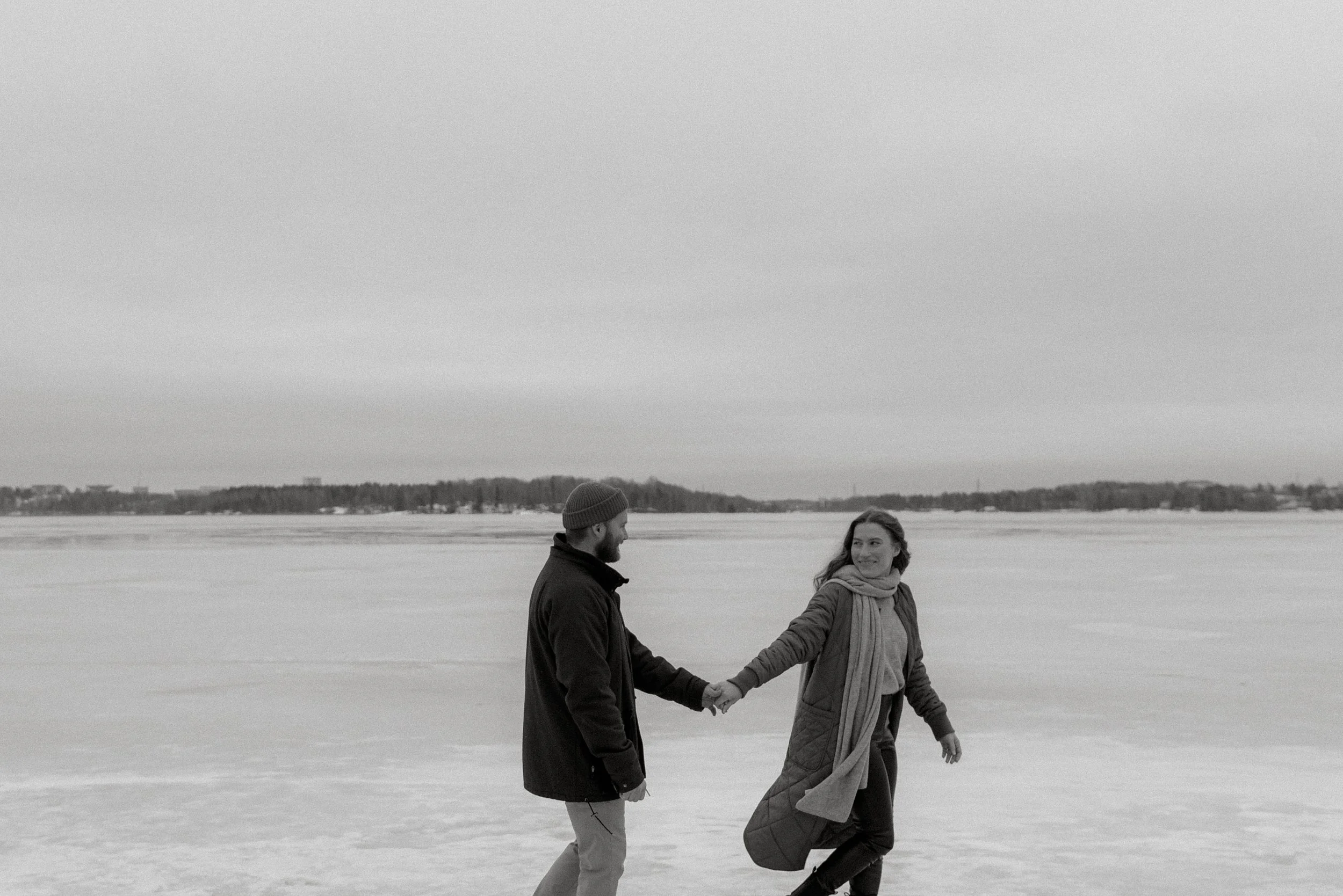 Pariskuntakuva, jossa nainen ja mies kävelevät käsi kädessä järven jäällä.