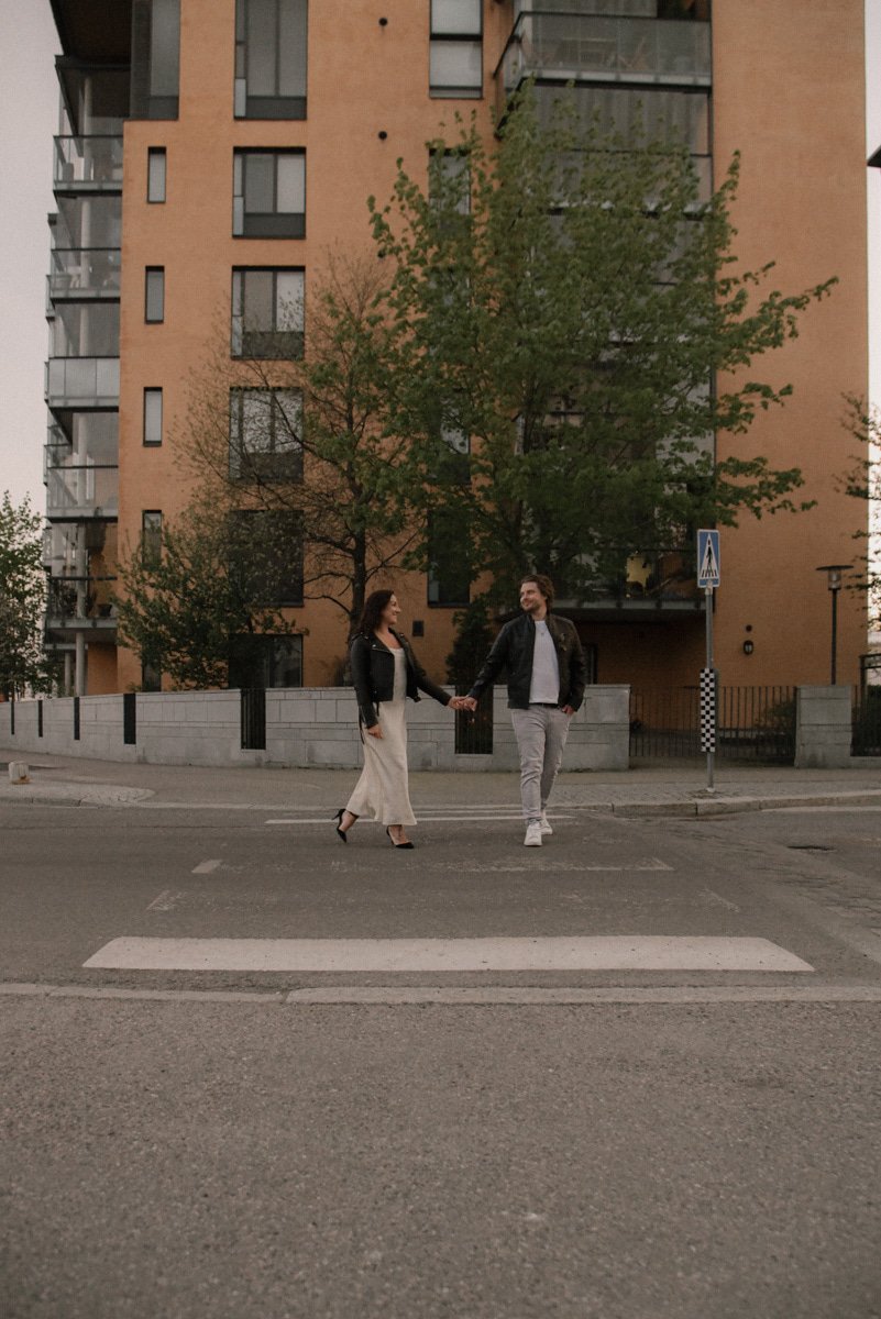 Pariskunta ylittää tietä käsi kädessään. Pariskuntakuvaus Espoo.