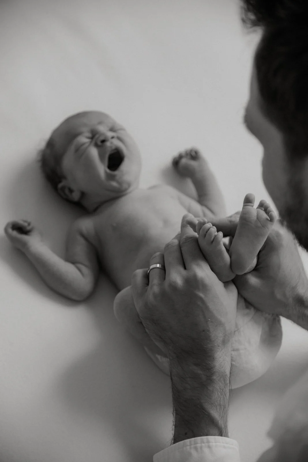 Vastasyntynyt vauva, isä pitelee käsillään vauvan varpaista. Kuvan on ottanut vauvakuvaaja Heidi Väisänen.