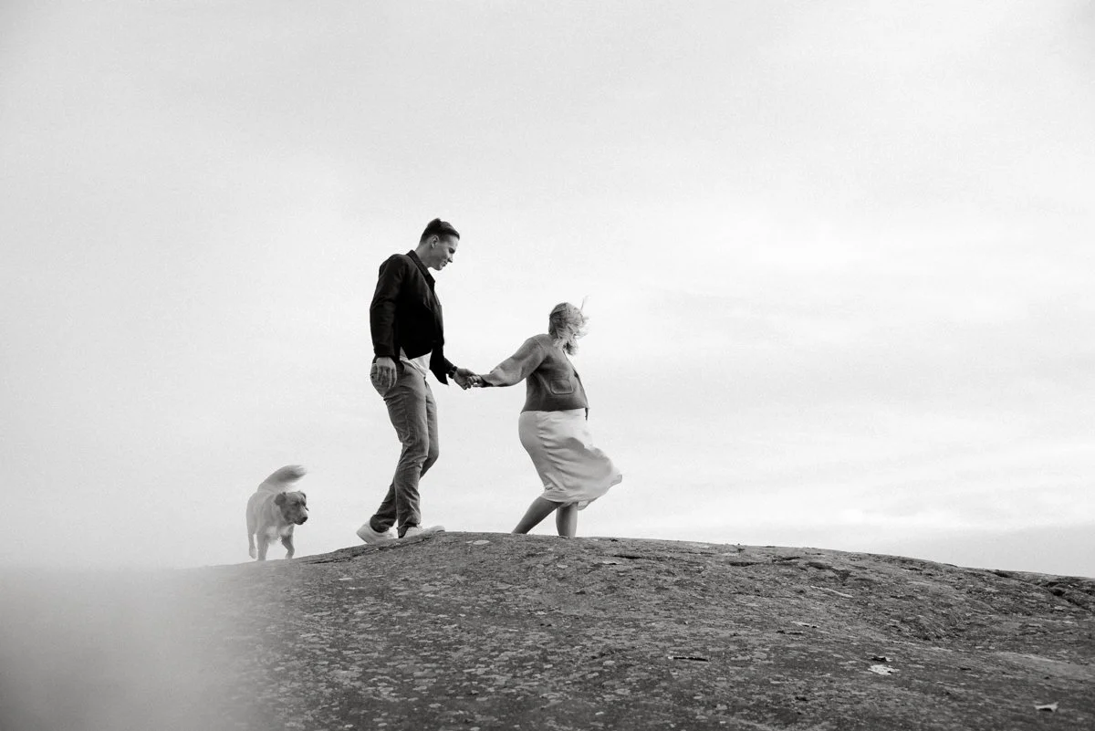 Odotusajankuvauksessa Isä, odottava äiti ja koira kävelevät kalliolla yhdessä.