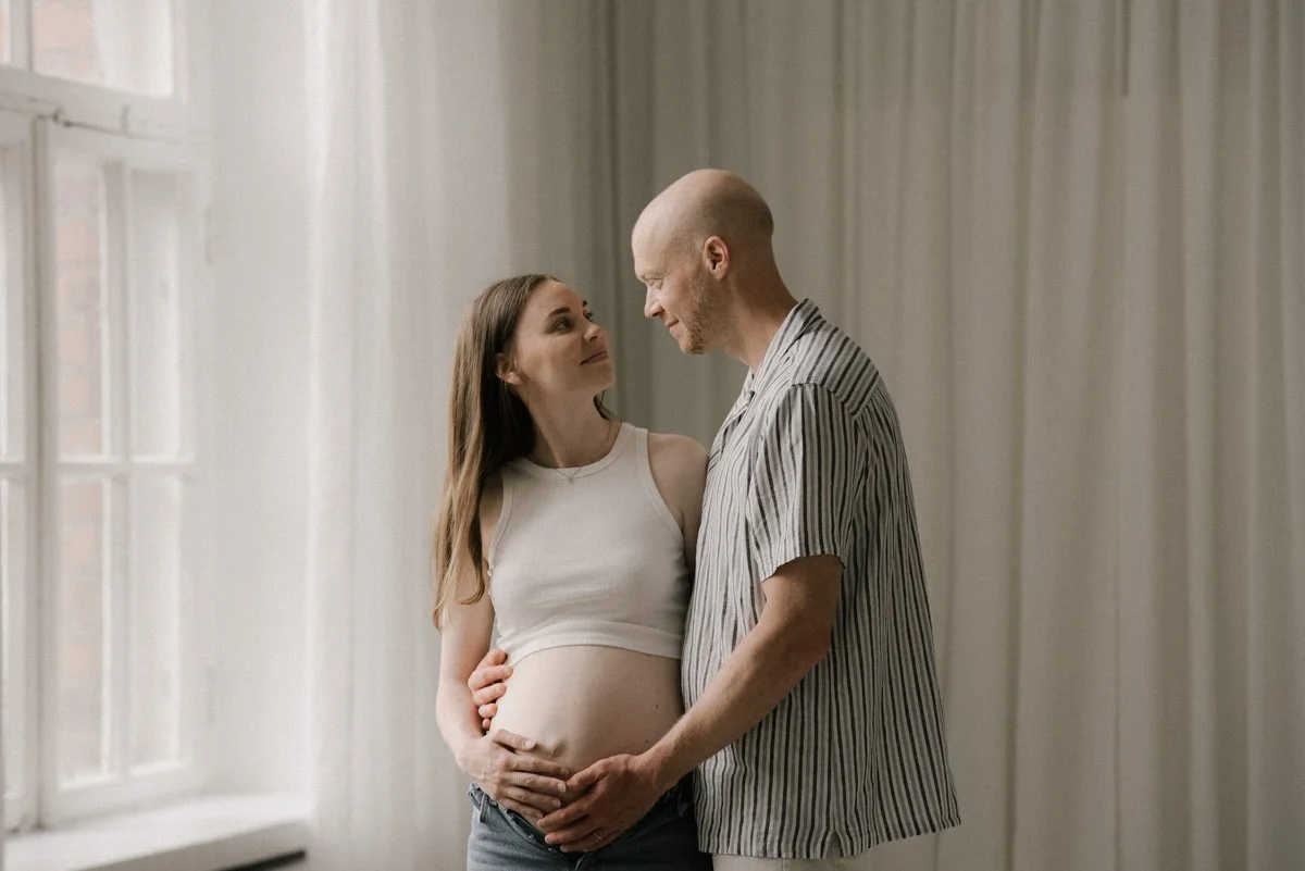 Odottava äiti ja isä läheisessä syleilyssä. Odotusajankuvaus on toteutettu Heidi Väisäsen studiolla Keravan Saviossa.