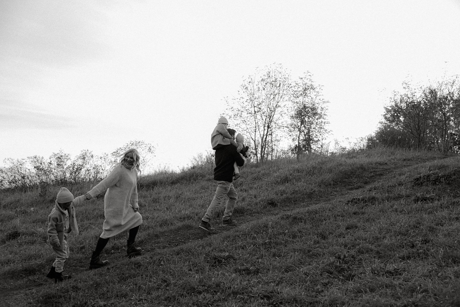 Perhekuvaus miljöössä, isä kävelee edellä pieni lapsi olkapäillään, äiti perässä käsikkäin toisen pienen lapsen kanssa. Kuvannut valokuvaaja Heidi Väisänen.