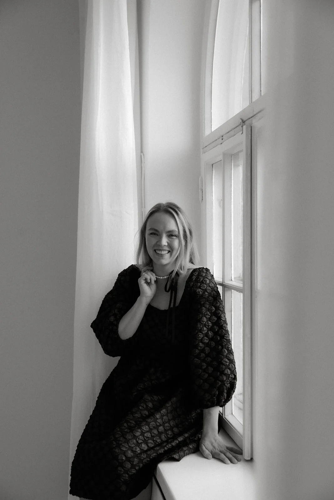 Yrityskuvaus studiolla. Yrittäjä istuu ikkunalaudalla ja katsoo hymyillen kameraan.