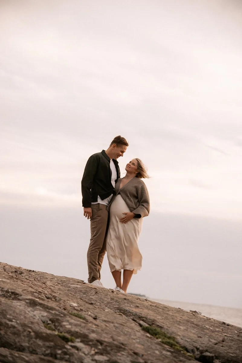 Pariskunta nojautuneena toisiinsa kalliolla. Raskauskuvaus Espoo.