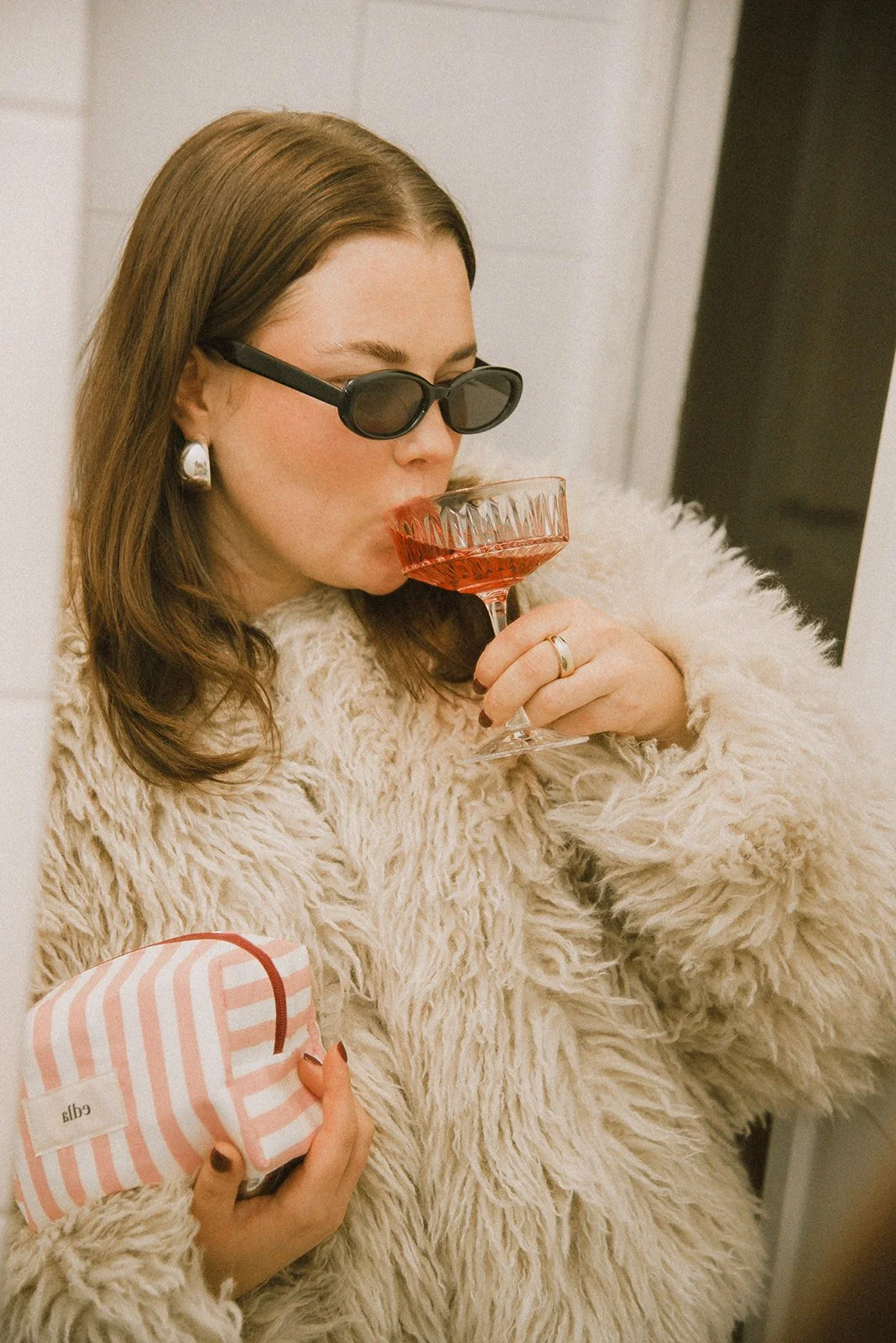 Edlan brändikuvaus, yrittäjä siemailee drinkkiä brändin meikkipussi kainalossaan.