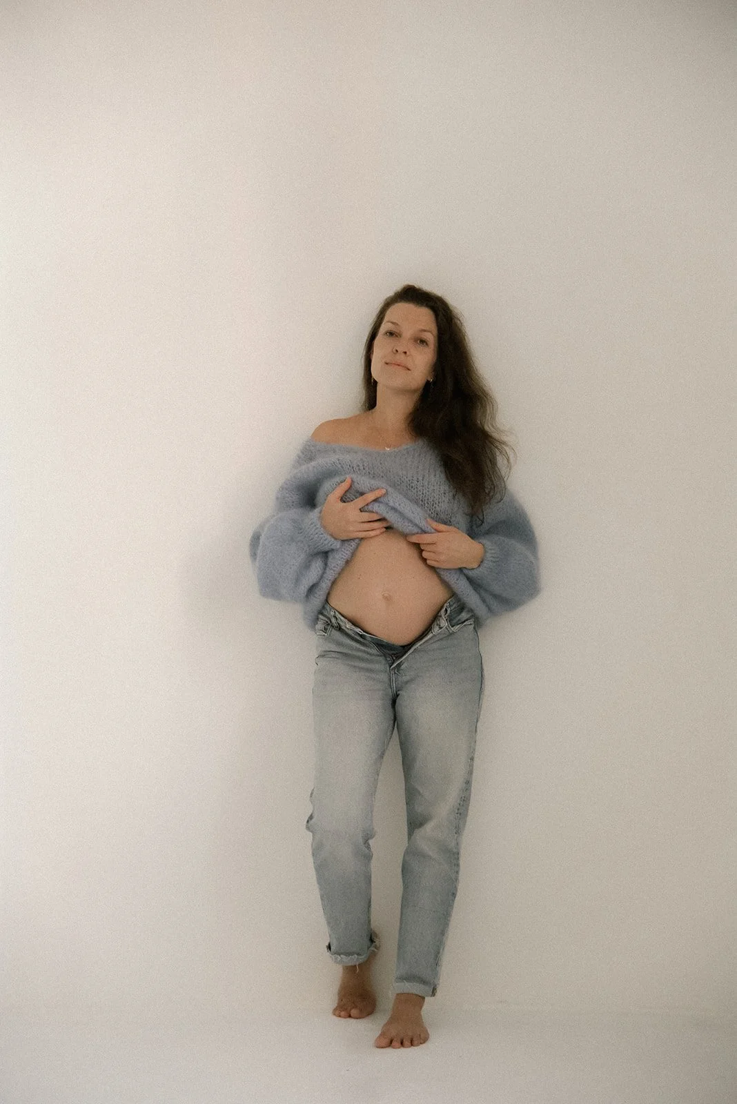 Odotusajankuvaus, jossa äiti nojaa seinään ja pitelee neuletta ylhäällä, jotta vatsa näkyy.