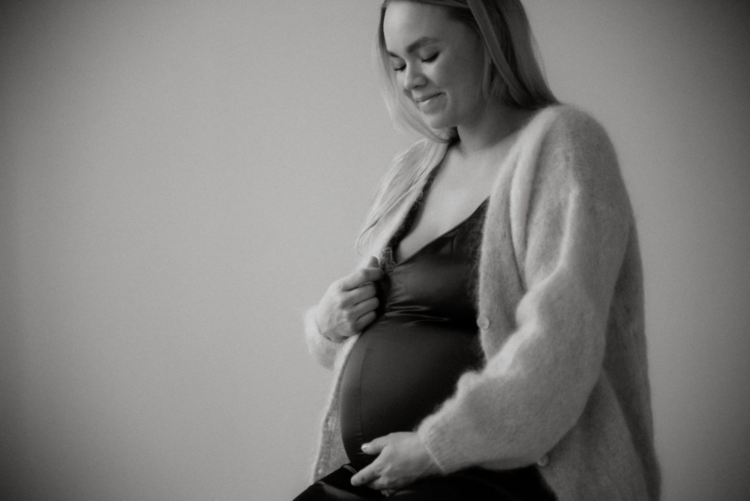 Äiti katsoo alas vatsaansa mustavalkoisessa kuvassa. Odotuskuvaus studiolla.