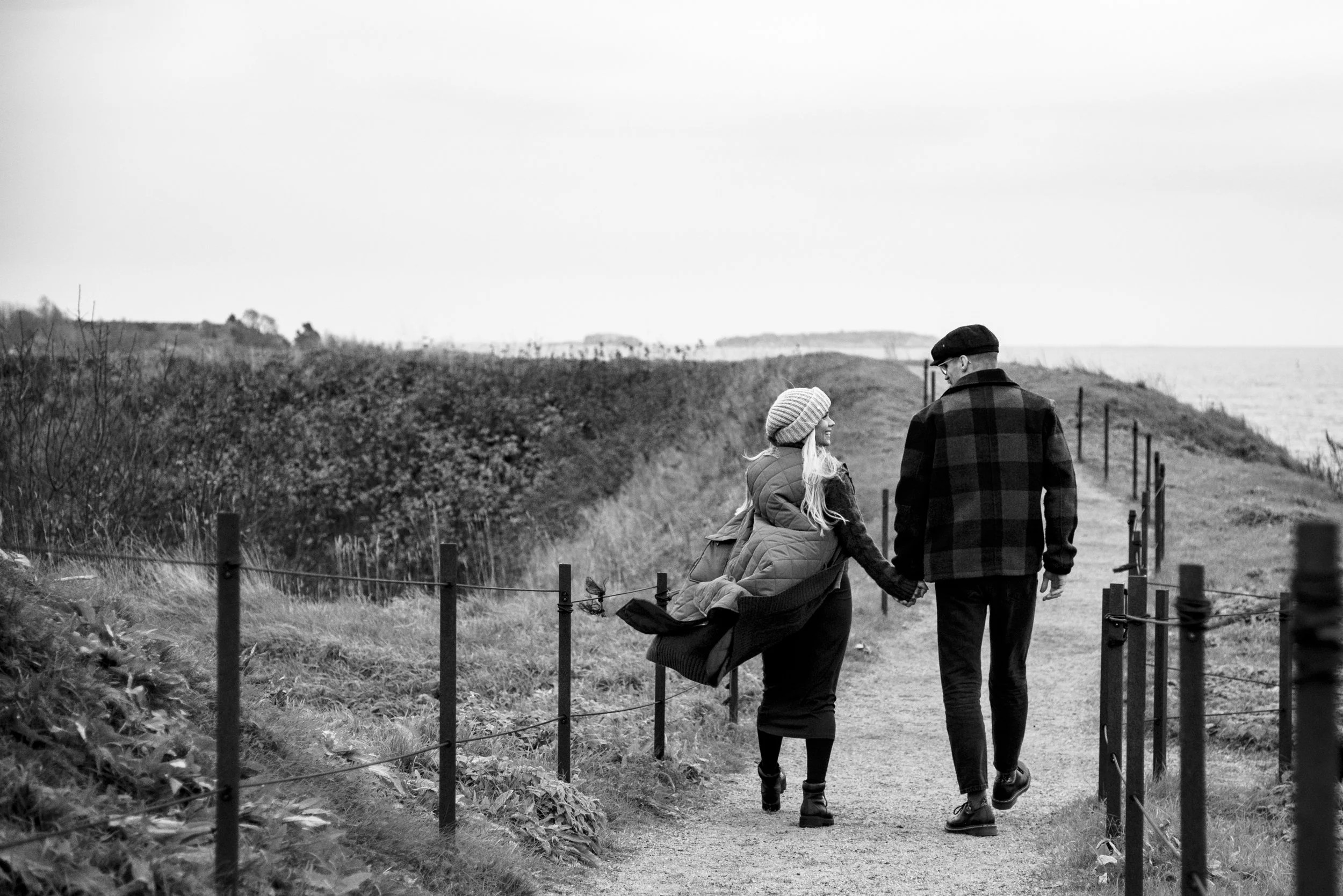 Heidi Väisäsen kuvaama mustavalkoinen otos, jossa pariskunta kävelee hiekkatiellä. Odotusajankuvaus Suomenlinna.
