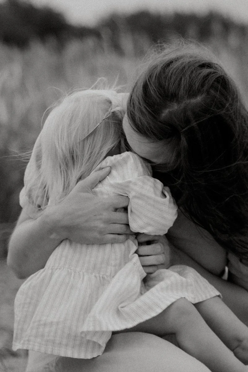 Mustavalkokuva äidistä ja lapsesta halaamassa, taustalla luontomaisema.