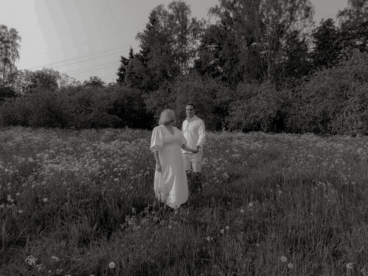 Mustavalkokuva pariskunnasta kävelemässä käsi kädessä kauniilla niityllä.