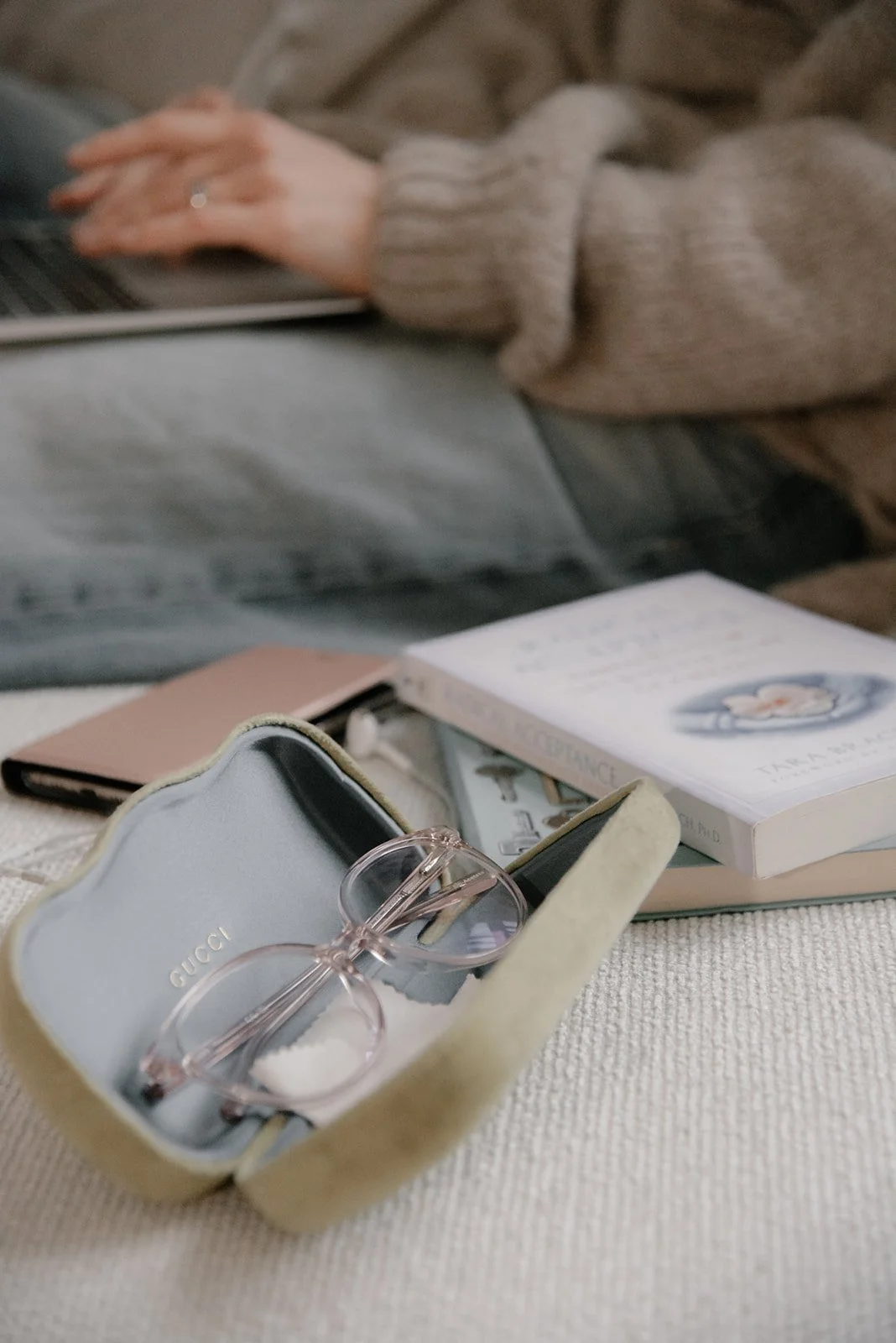 Silmälasit kotelossaan ja pino kirjoja, taustalla Vaumiin Miia naputtelee tietokonetta.