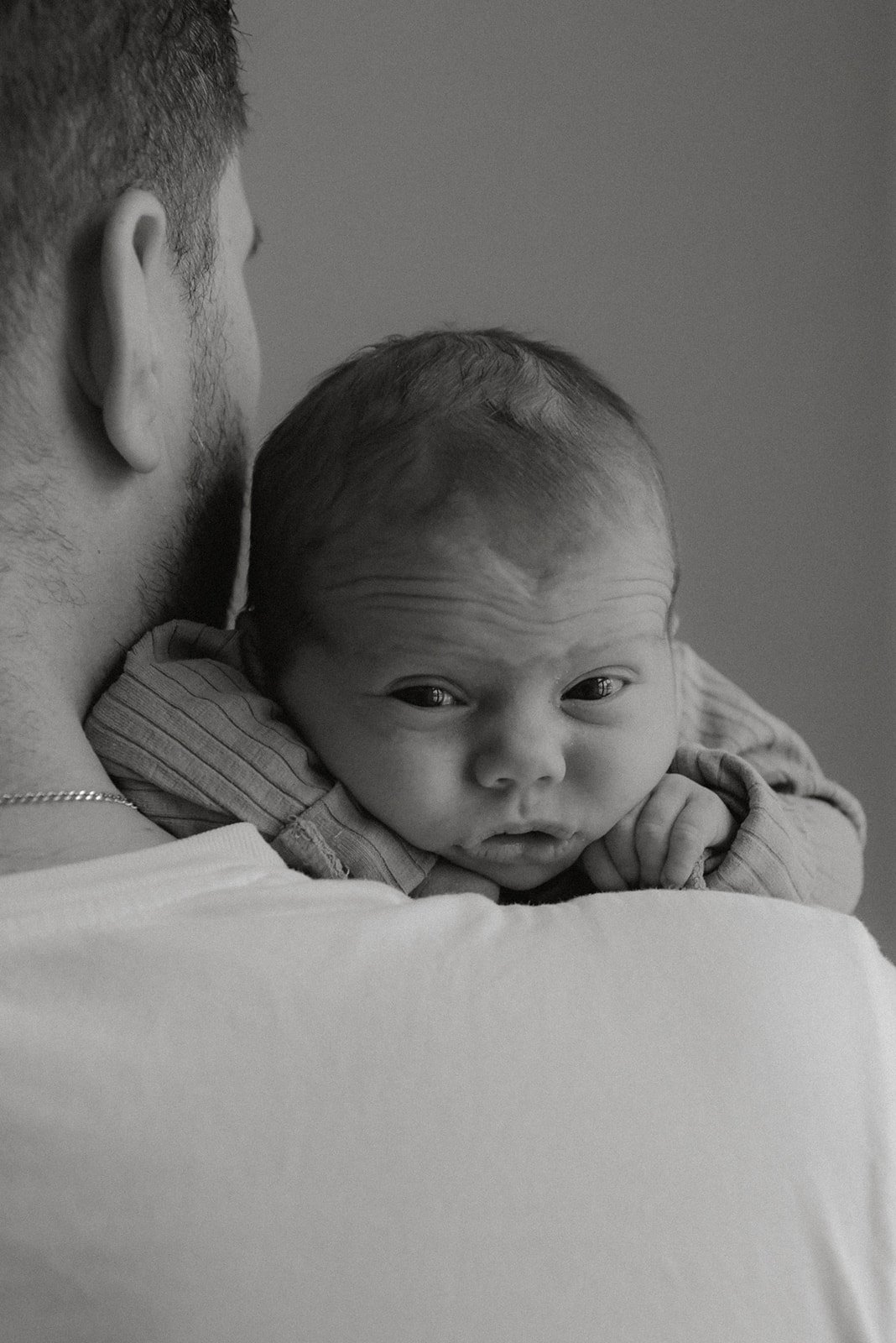Vastasyntyneen kuvaus, vauva katselee isän olkapään yli.
