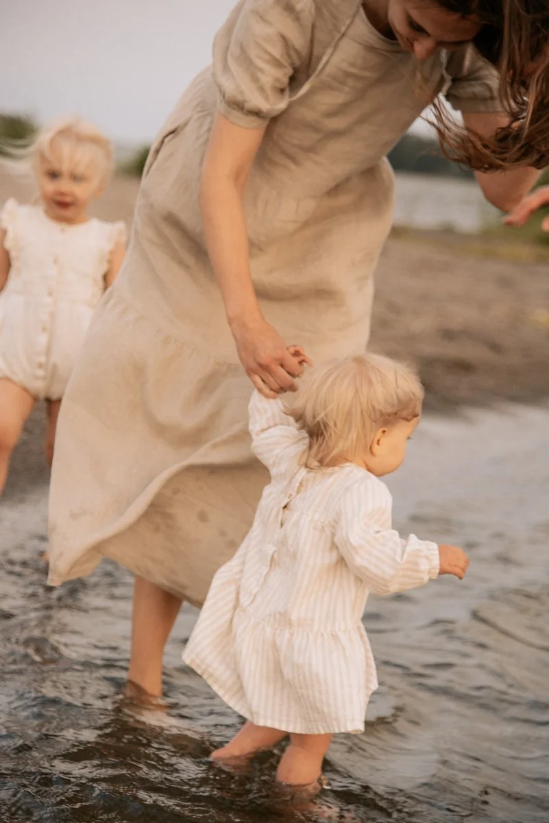 Perhekuvaus miljöössä, äiti ja kaksi pientä lasta kahlaa vedessä. Kuvannut valokuvaaja Heidi Väisänen.