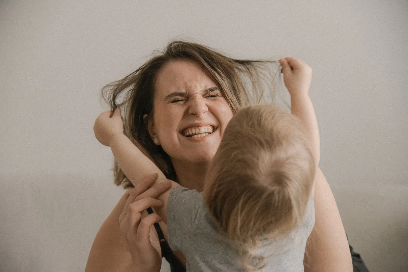 Lapsi leikkii riemukkaasti äidin hiuksilla. Perhekuvaus Espoo.