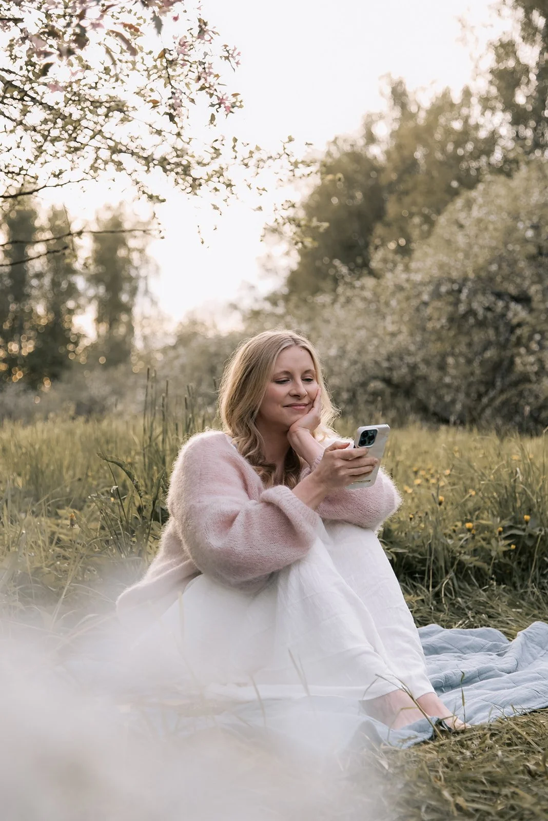 Brändikuvaus luonnon keskellä. Naisyrittäjä istuu niityllä viltin päällä ja selaa puhelintaan.