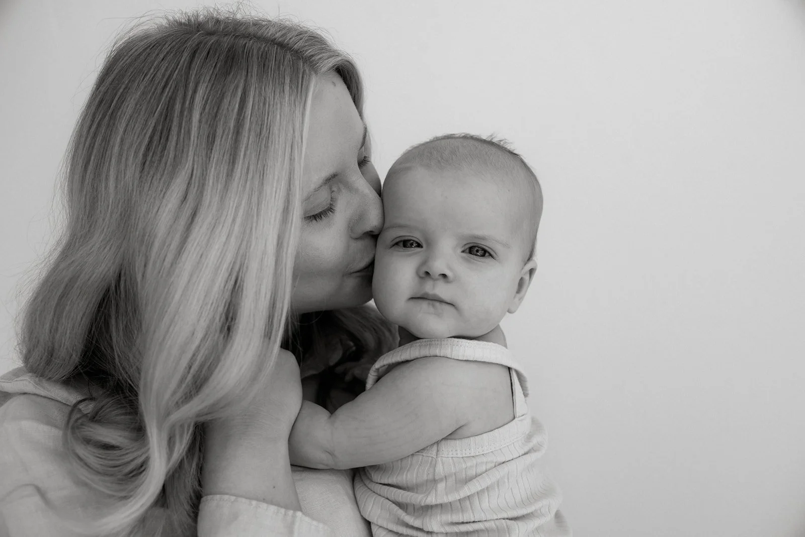 Heidi Väisäsen toteuttamat kuvaukset studiolla. Äiti suukottaa vauvaa poskelle.