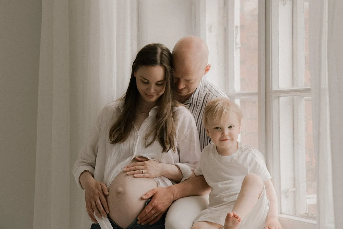 Perhekuva, jossa odottava äiti perheineen valoisassa studiossa Keravalla.