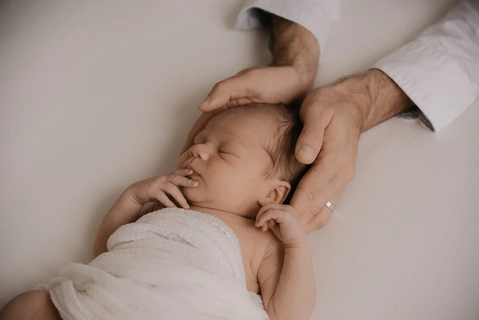 Vastasyntynyt vauva nukkuu, isä pitelee hellästi päästä kiinni. Kuvan on ottanut vauvakuvaaja Heidi Väisänen.