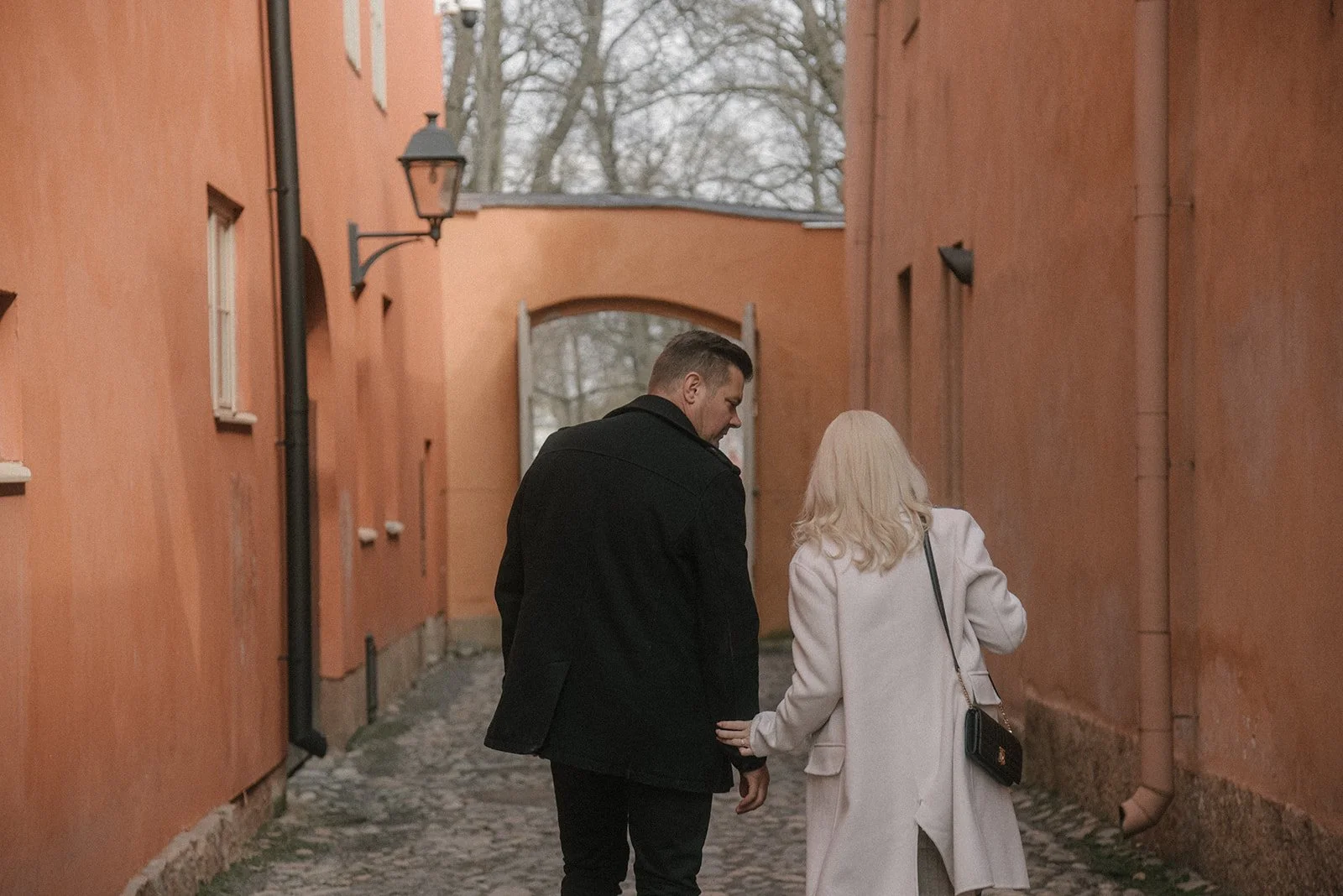 Pariskunta kävelee pitkin kapeaa katua kaupunkimaisemassa. Pariskuntakuvaus Helsinki.