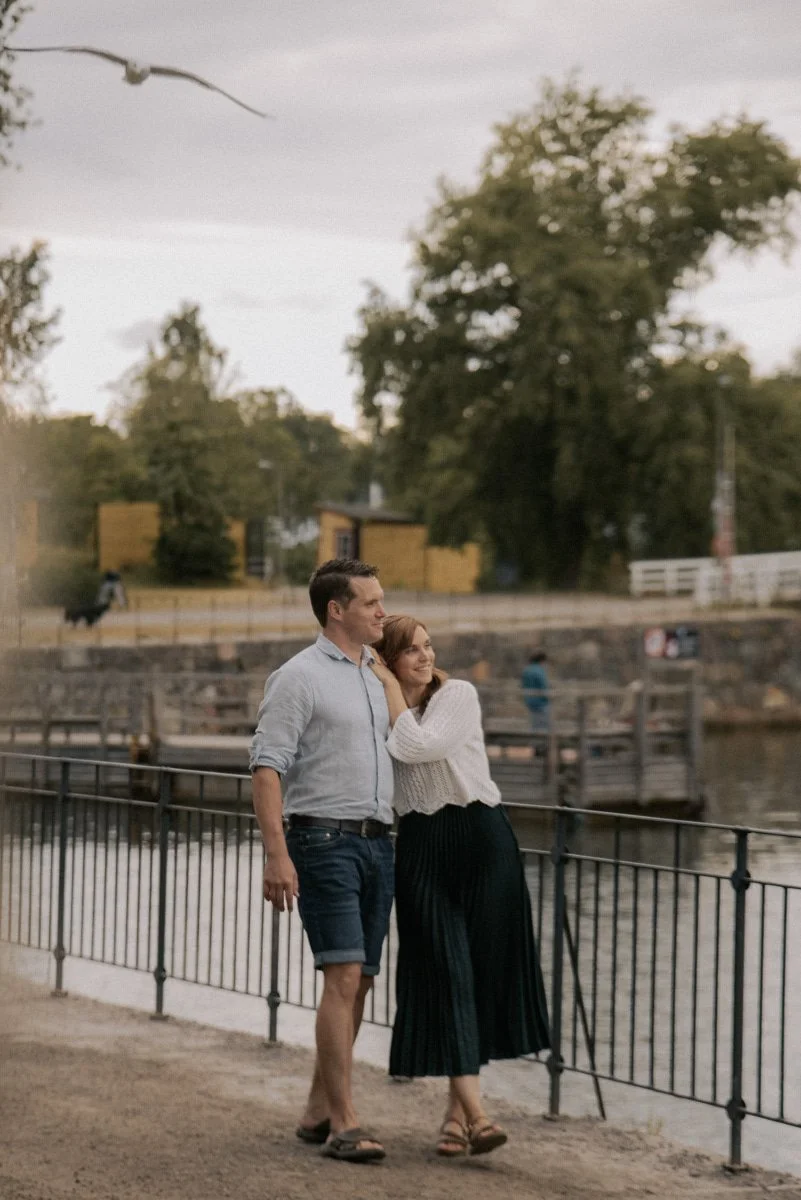 Pariskunta nojaa toisiinsa, taustalla vettä ja luontoa.