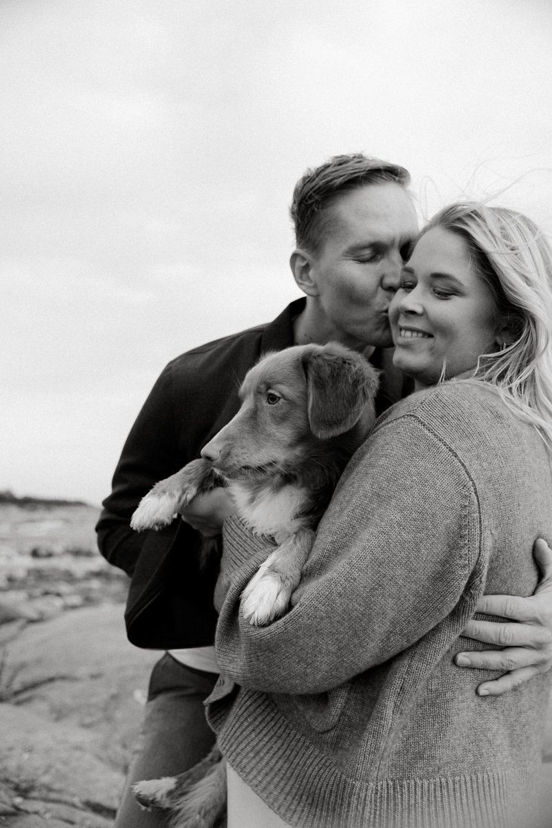 Perheen hellässä syleilyllä isä, äiti ja koira. Raskauskuvaus miljöössä.