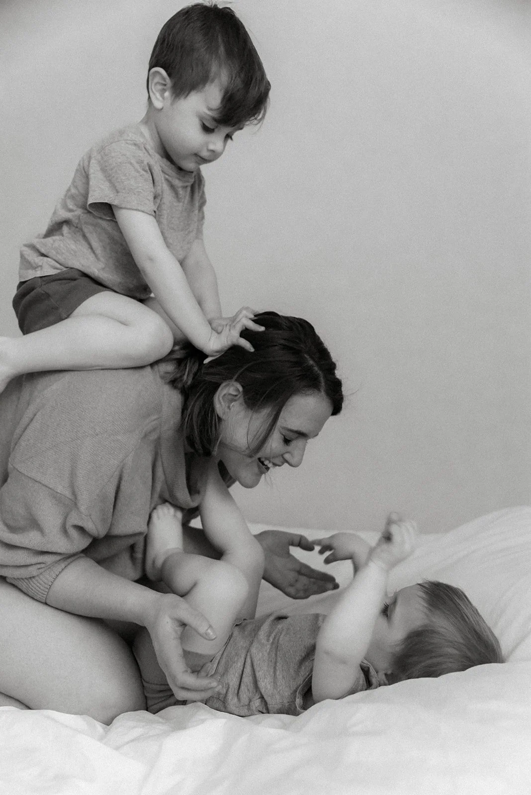 Äiti leikkii iloisesti lastensa kanssa sängyllä. Perhekuvaus Espoo.