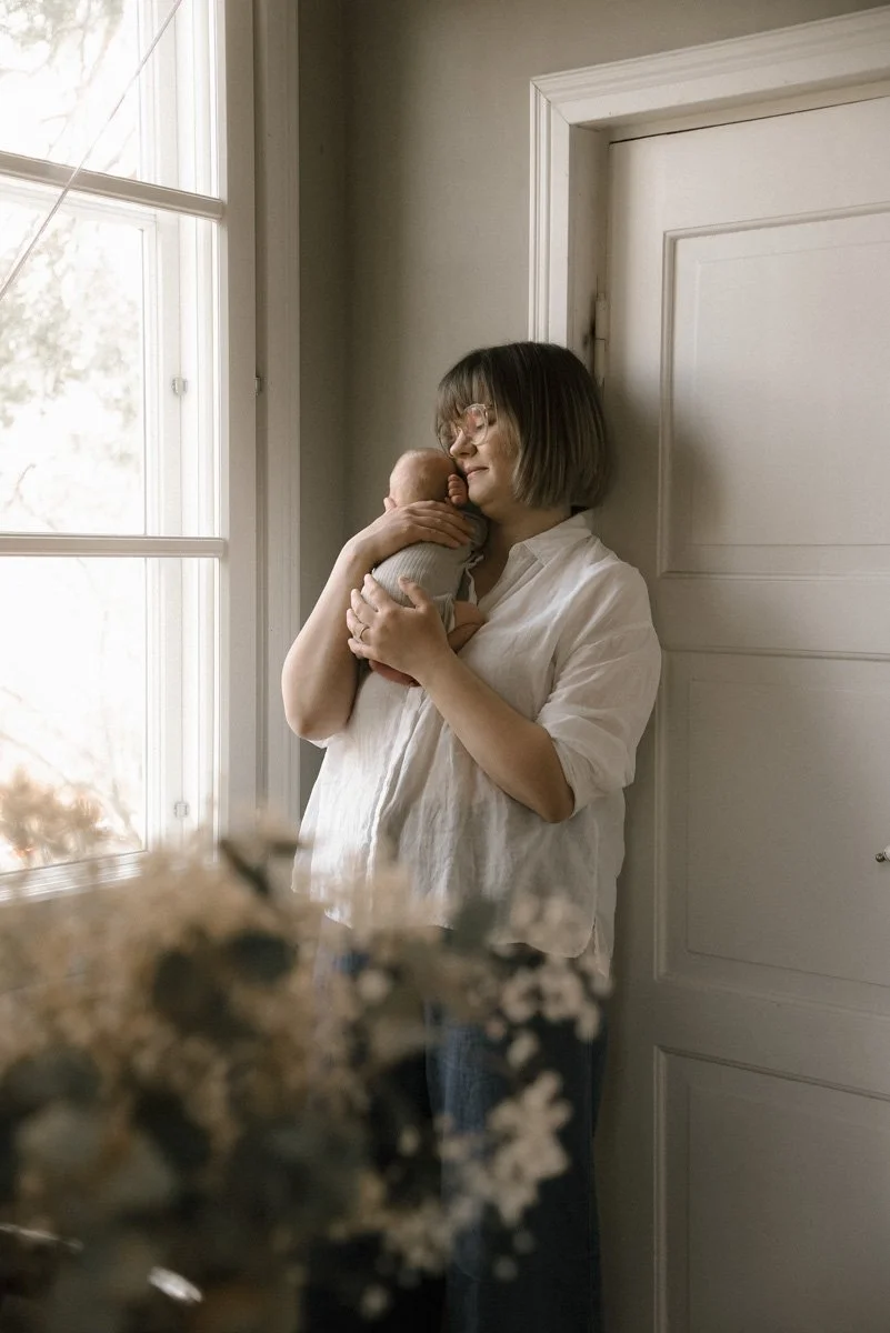 Äiti pitelee vauvaa sylissään valoisassa kodissa.  Perhekuvaus kotona, kuvannut Heidi Väisänen.
