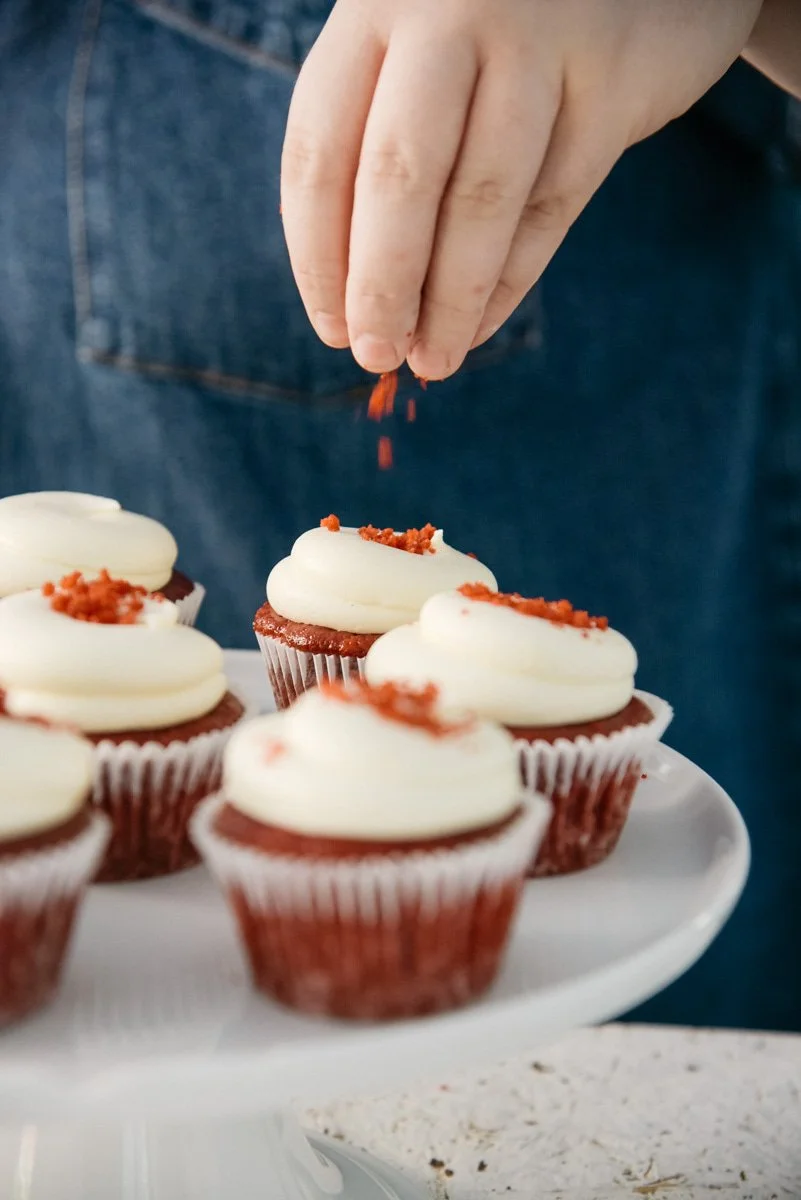 Herkullinen tuotekuva, jossa yrittäjä ripottelee koristeita kuppikakkujen pinnalle.