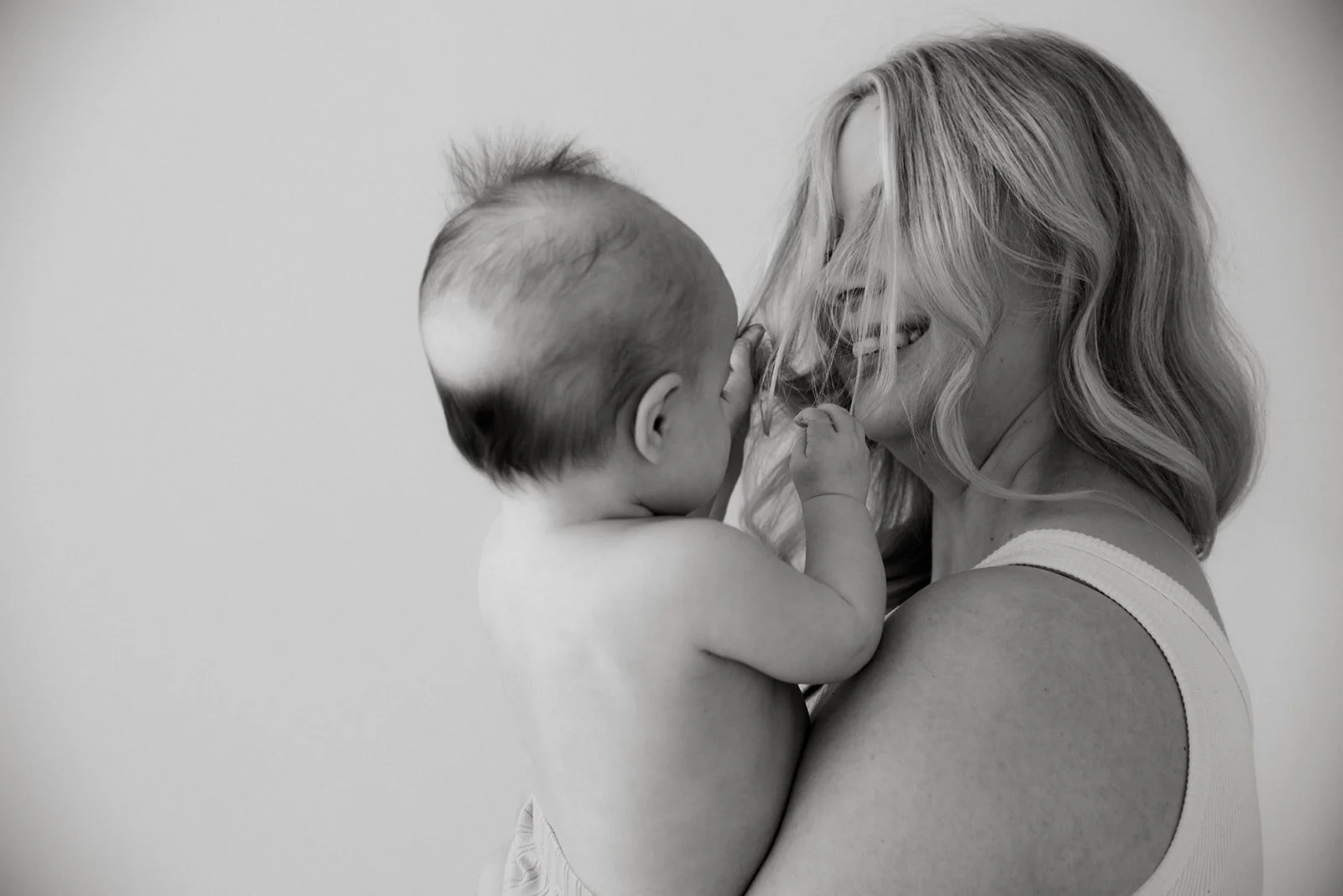 Pieni lapsi leikkii äidin hiuksilla. Äiti- ja lapsikuvaus Heidi Väisäsen studiossa Keravan Saviossa.